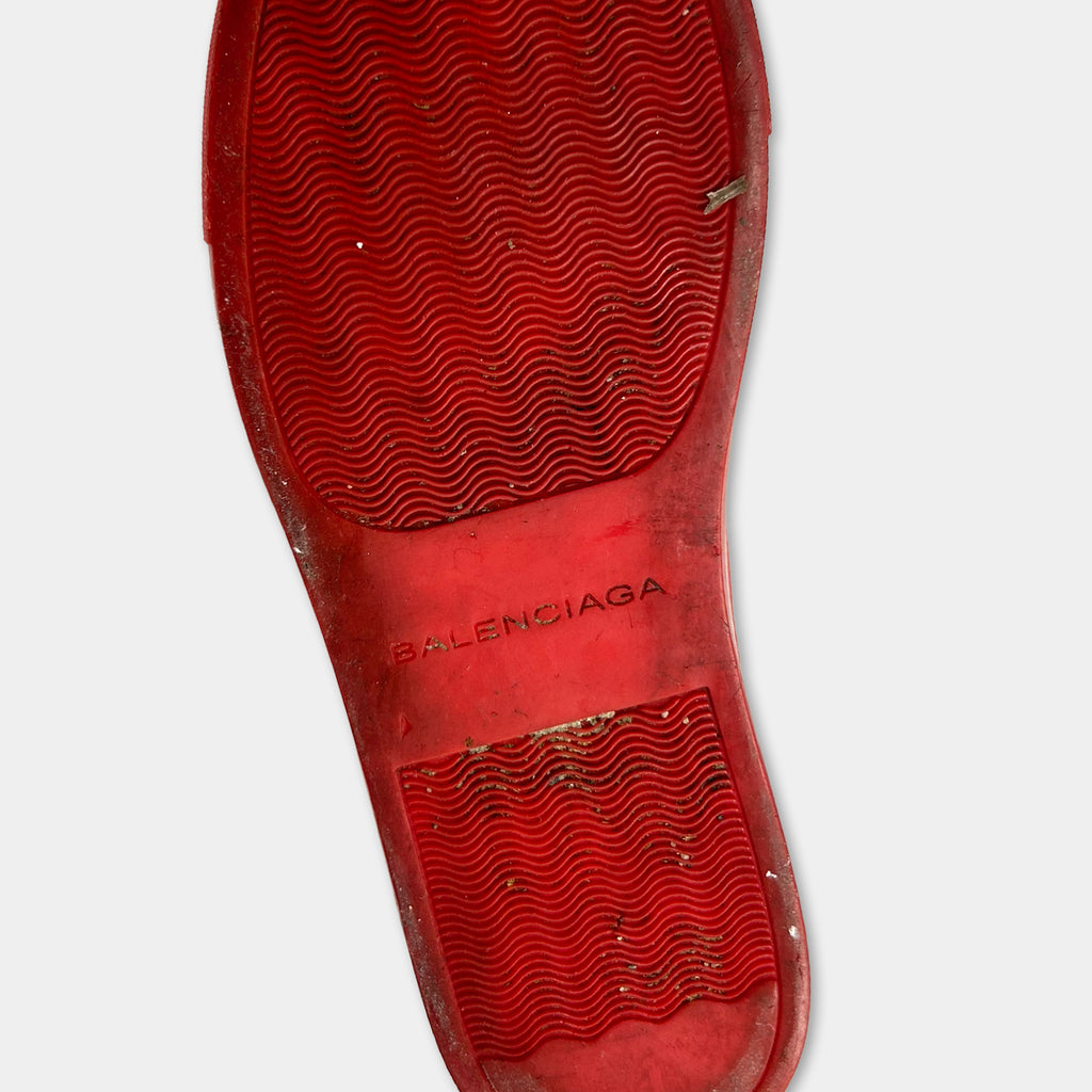 A close-up view of a red rubber sole with the Balenciaga logo printed on it.