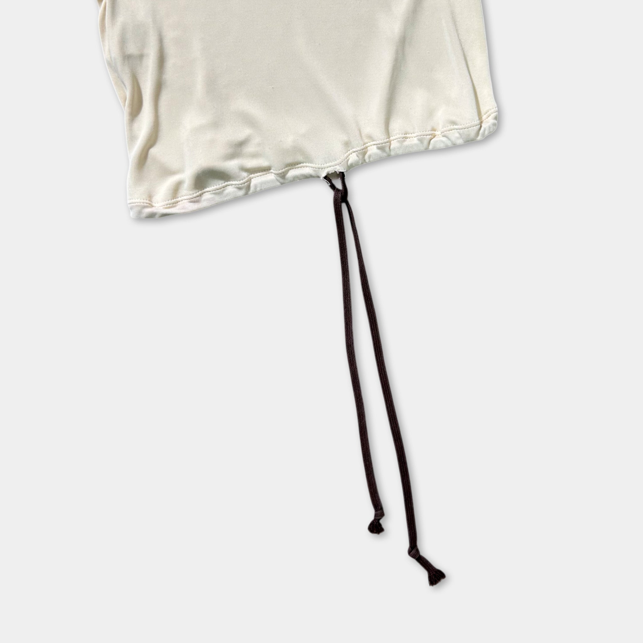 A white fabric with a black drawstring or tie attached to it, lying on a plain white background.
