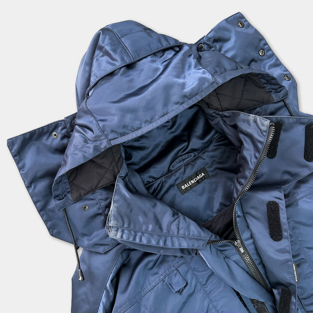 A close-up view of a navy blue jacket with a hood, zipper, and pockets, showing the details of the jacket's design.