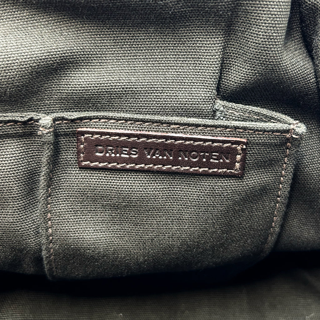 a close-up view of a dark grey fabric, possibly a canvas or leather material, with a small brown label or tag attached to it.