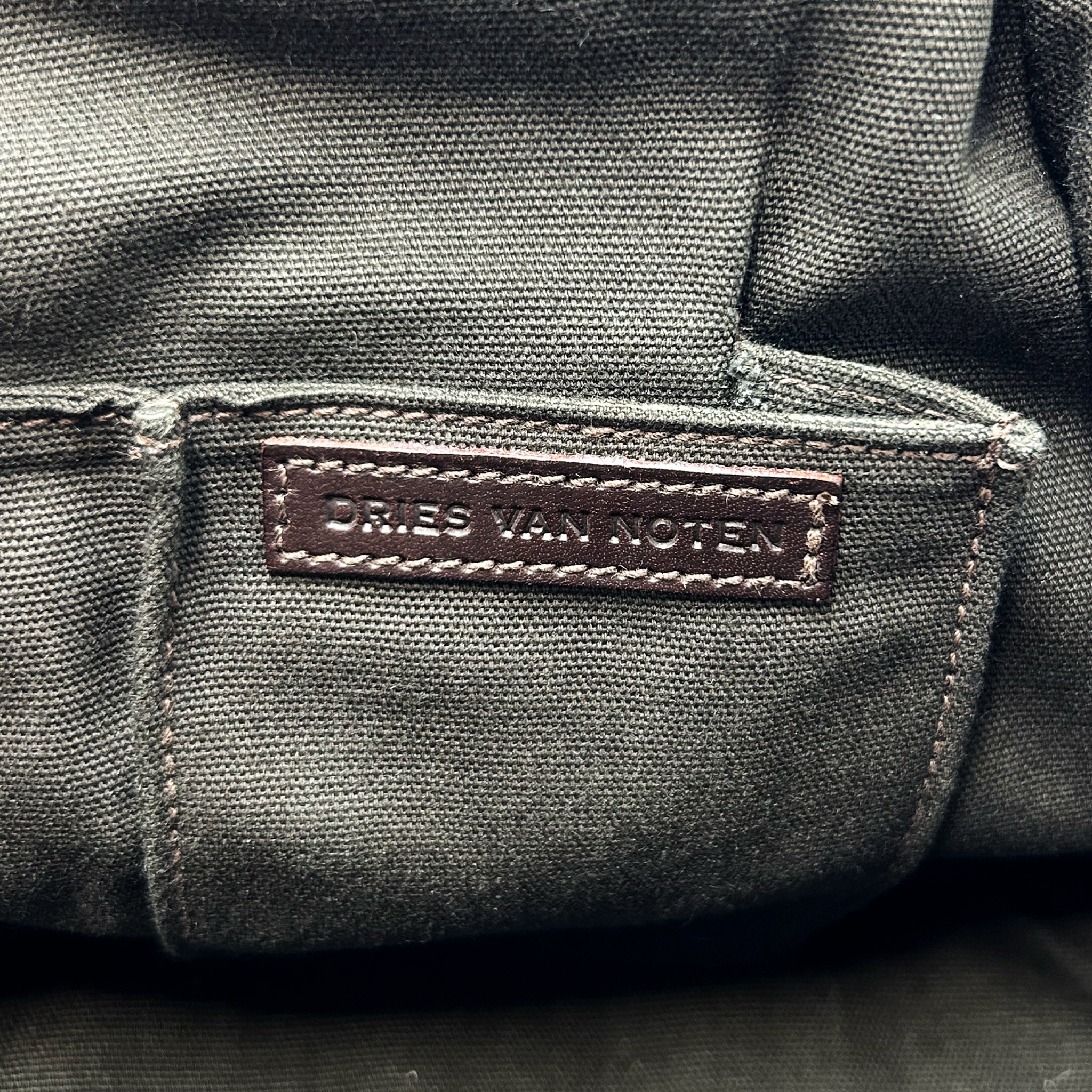 a close-up view of a dark grey fabric, possibly a canvas or leather material, with a small brown label or tag attached to it.