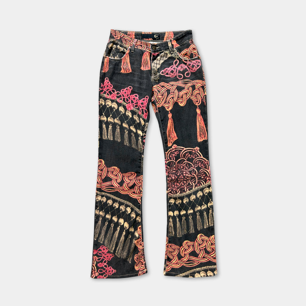 A pair of black jeans with a colorful, patterned design featuring tassels and floral elements.