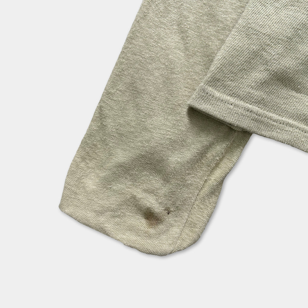 A close-up view of a beige fabric, possibly a sweater or garment, with a small stain on the bottom left corner.