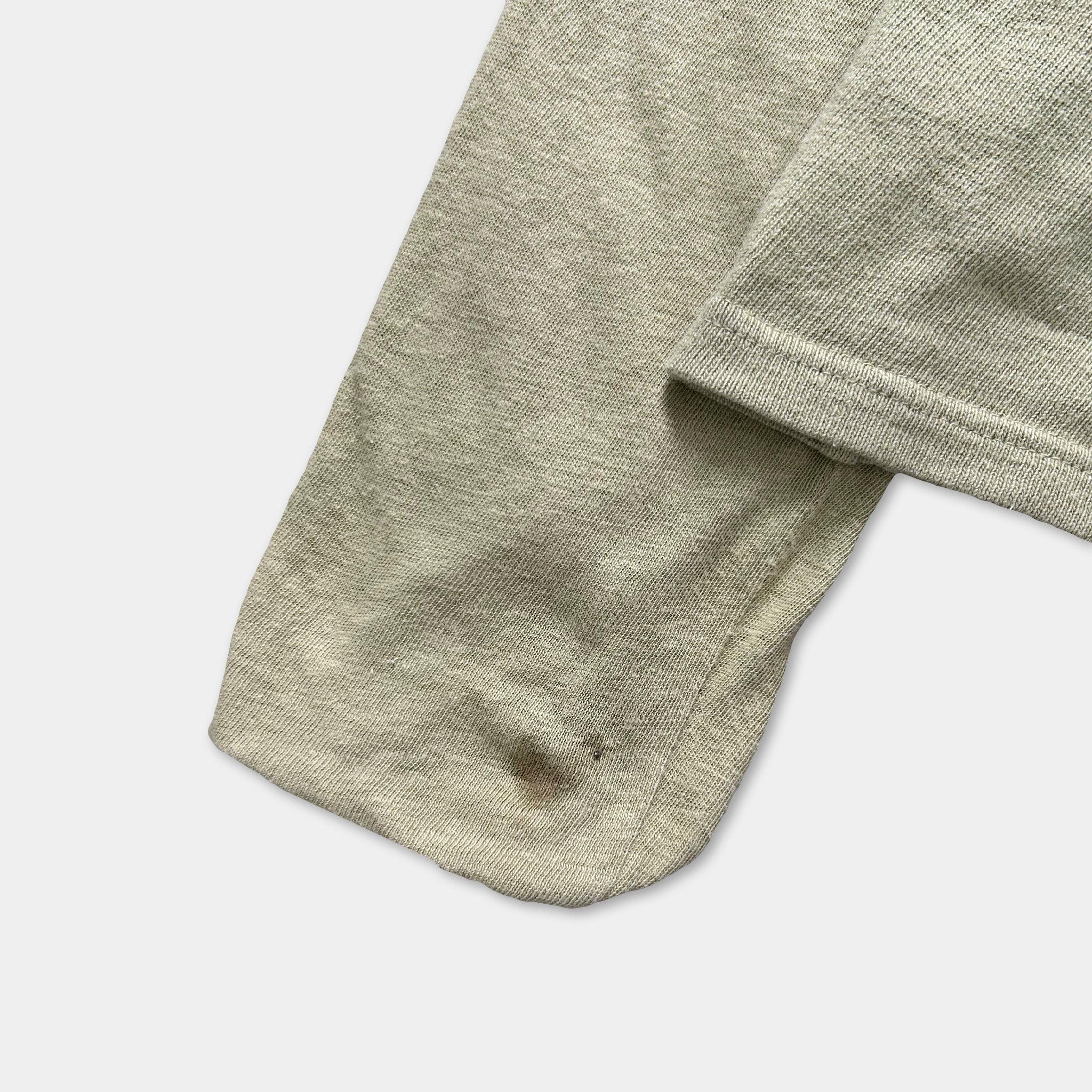 A close-up view of a beige fabric, possibly a sweater or garment, with a small stain on the bottom left corner.