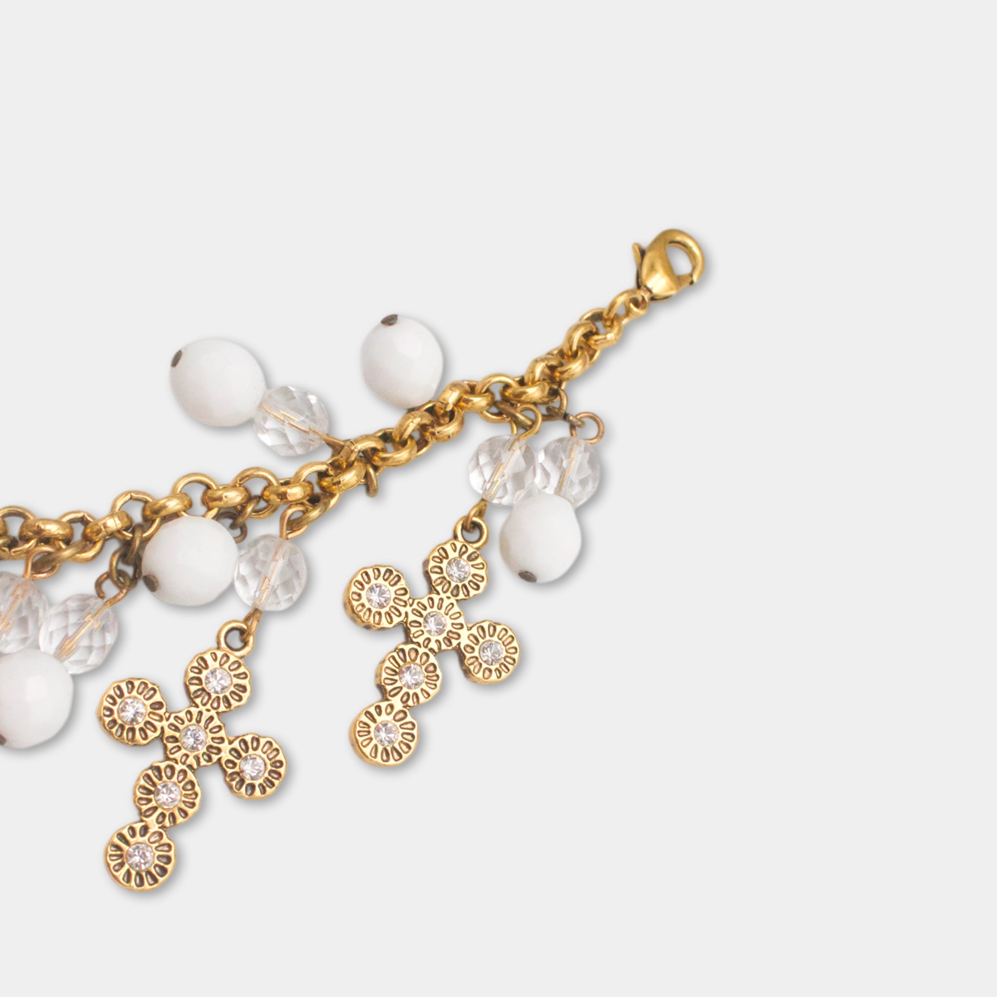 A gold-colored cross-shaped charm with white beads and clear beads hanging from it.