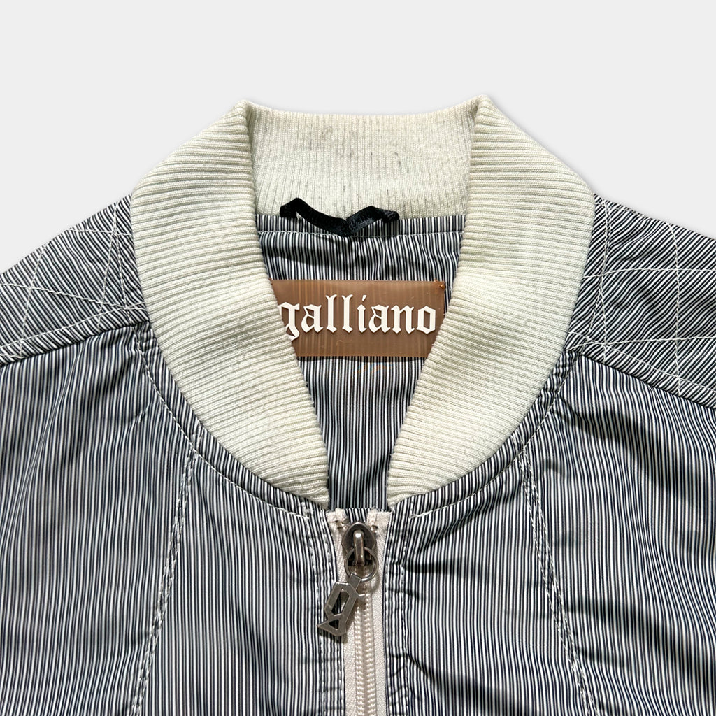 A close-up view of a striped jacket with a collar and zipper, featuring a label with the word "Galliano" printed on it.
