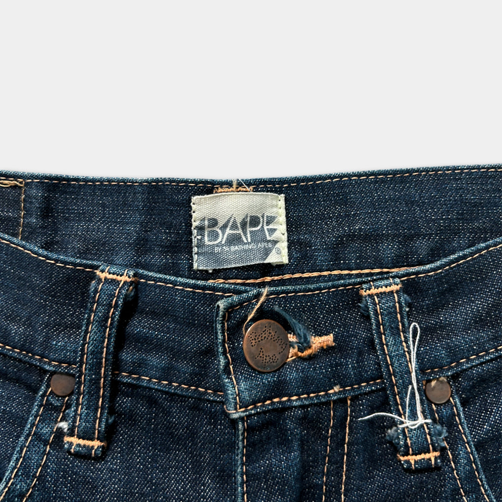 A close-up view of a pair of blue jeans, with a label on the waistband that reads "BAPE".