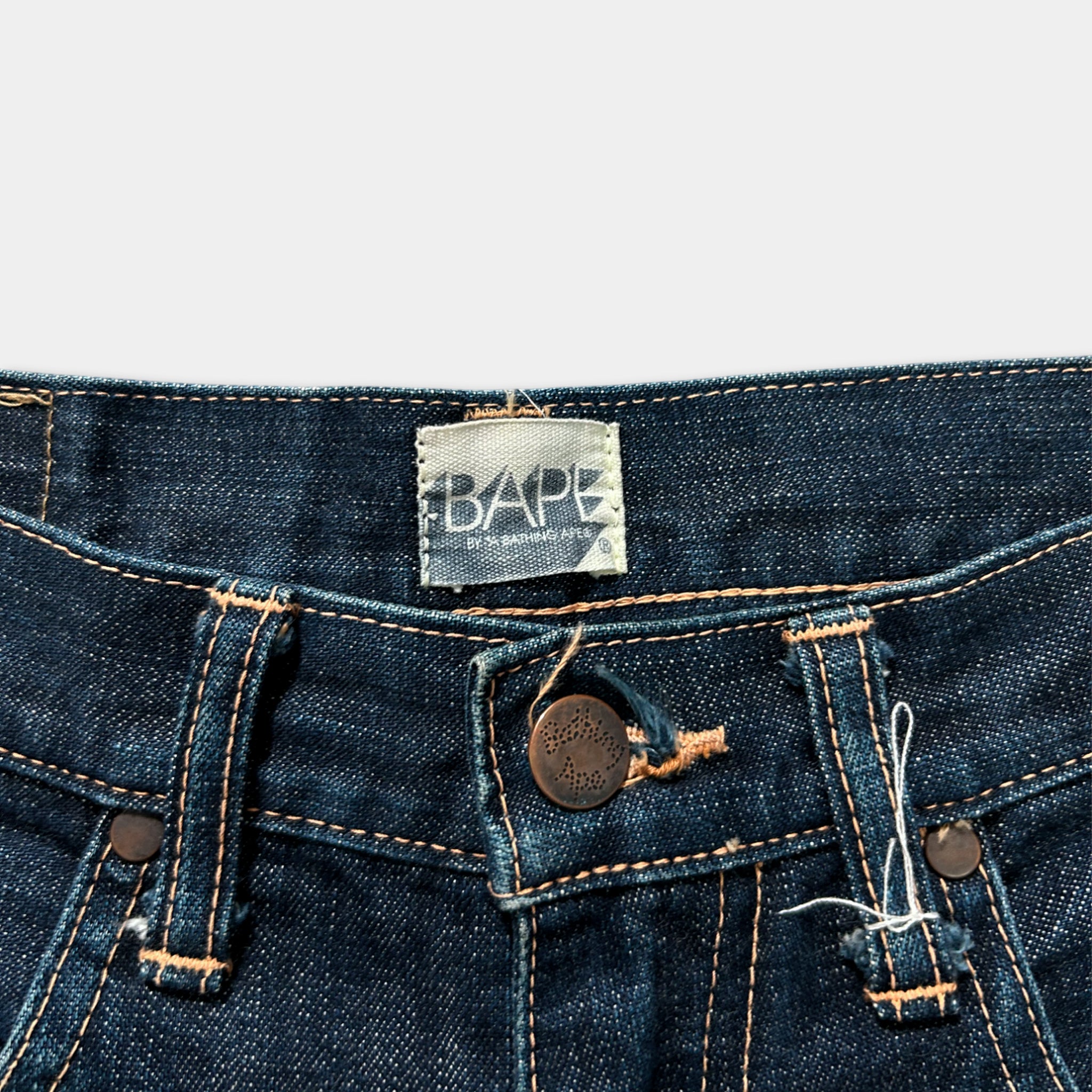 A close-up view of a pair of blue jeans, with a label on the waistband that reads "BAPE".