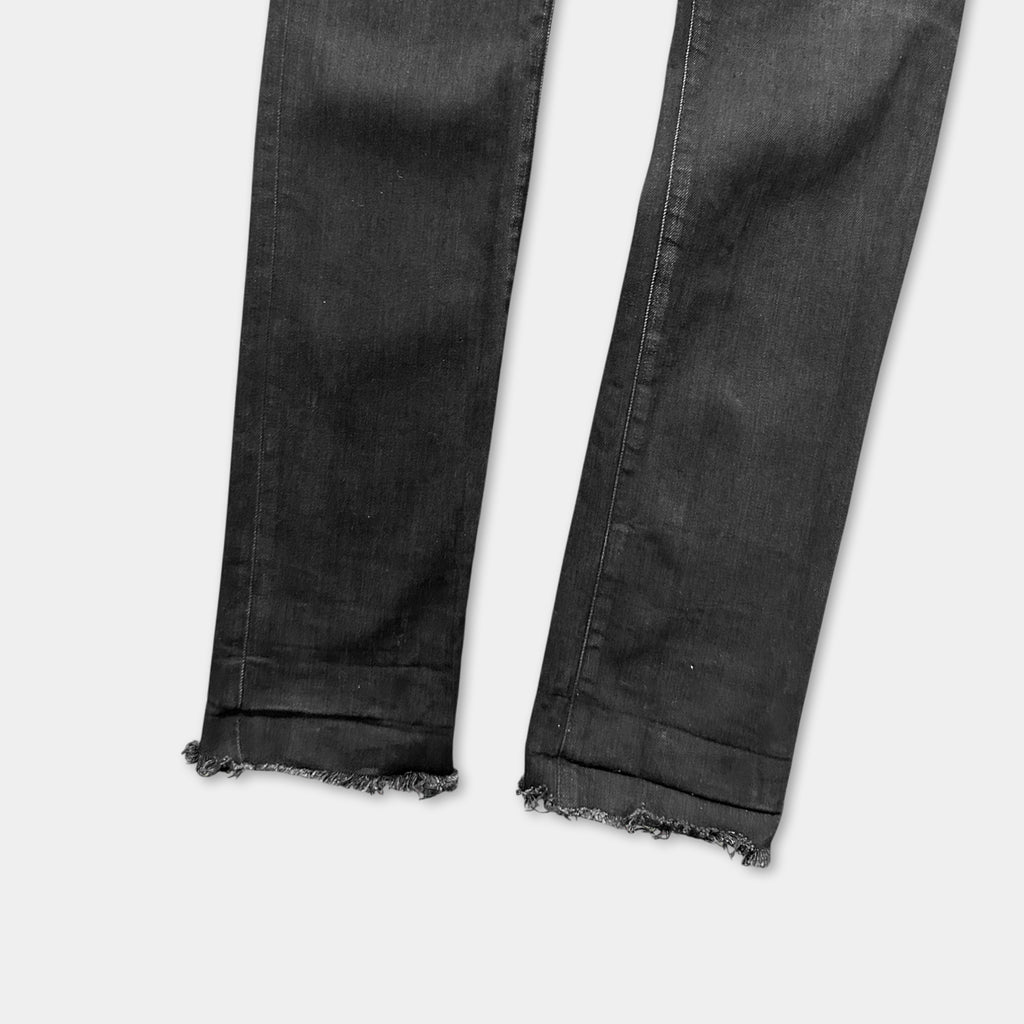 A pair of black jeans with frayed edges and a slightly worn appearance.