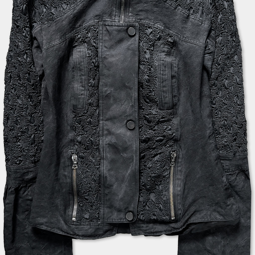 a close-up view of a black jacket with intricate lace-like patterns and multiple zippers.