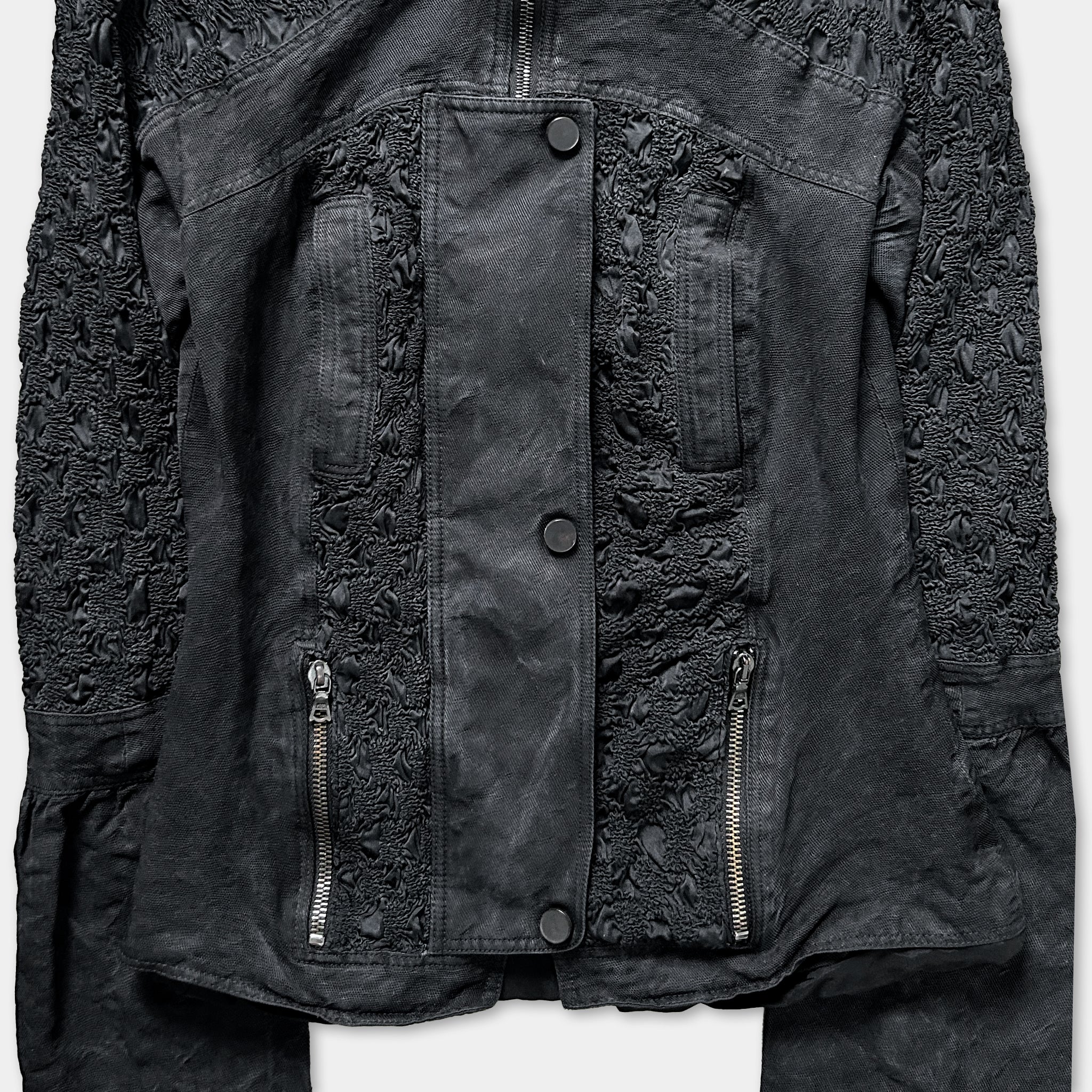 a close-up view of a black jacket with intricate lace-like patterns and multiple zippers.