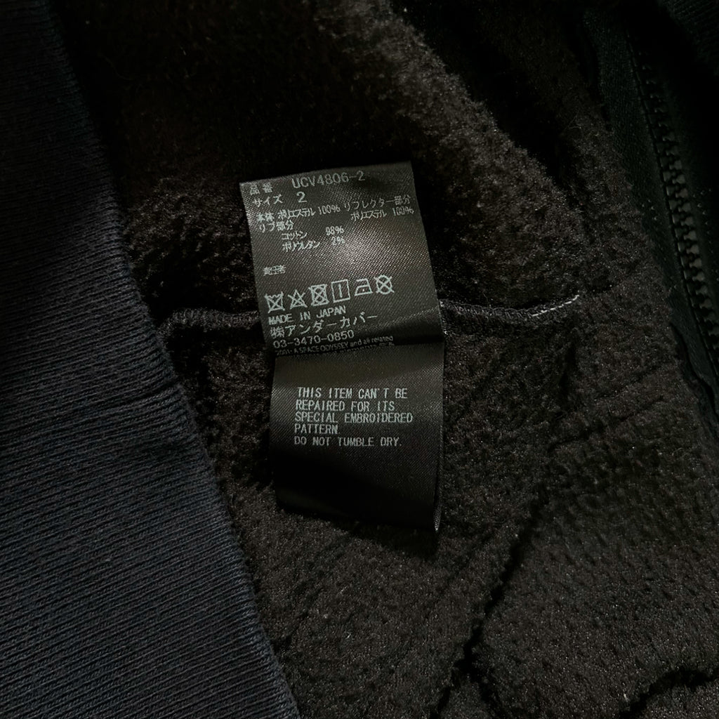 a close-up view of a black fabric, possibly a sweater or jacket, with a label attached to it. The label appears to contain information about the item, such as the brand, size, and care instructions.
