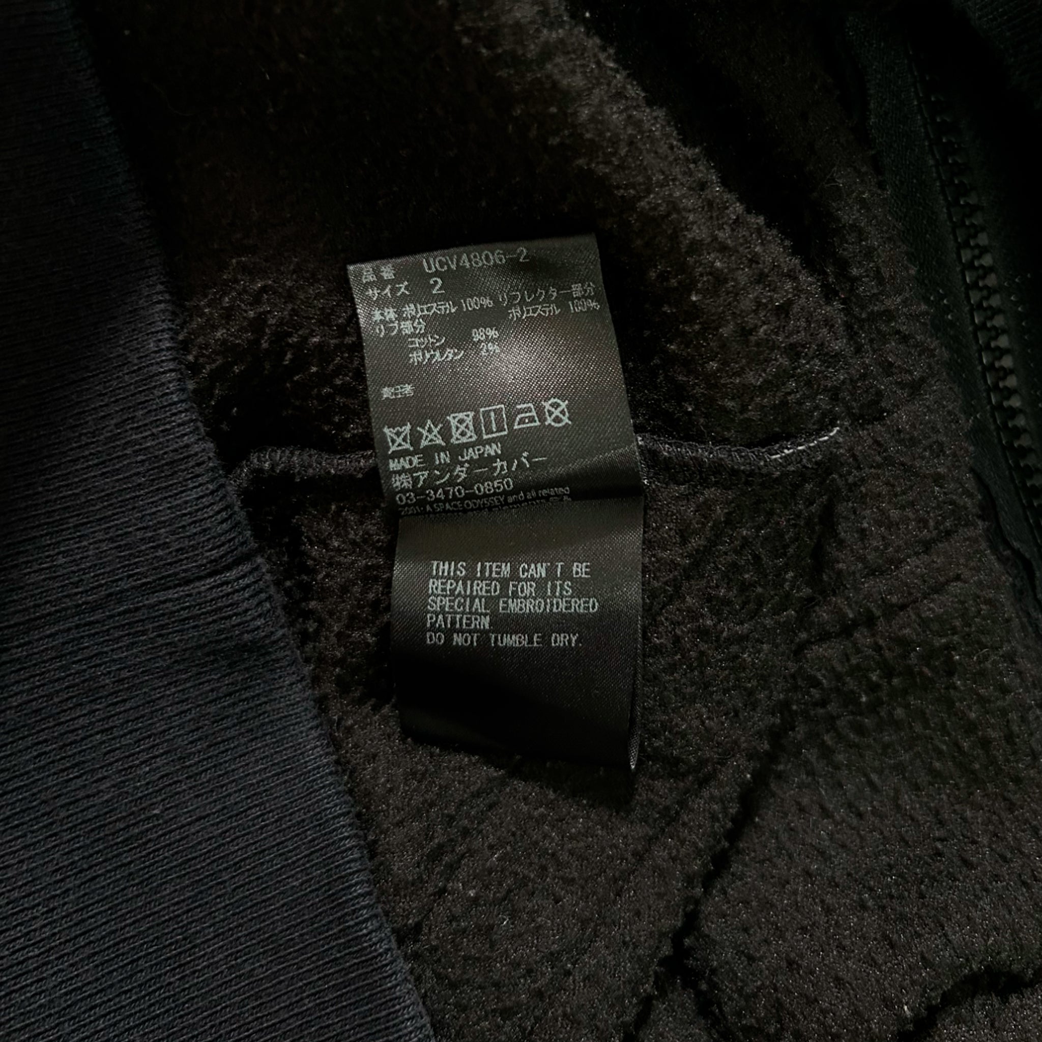 a close-up view of a black fabric, possibly a sweater or jacket, with a label attached to it. The label appears to contain information about the item, such as the brand, size, and care instructions.