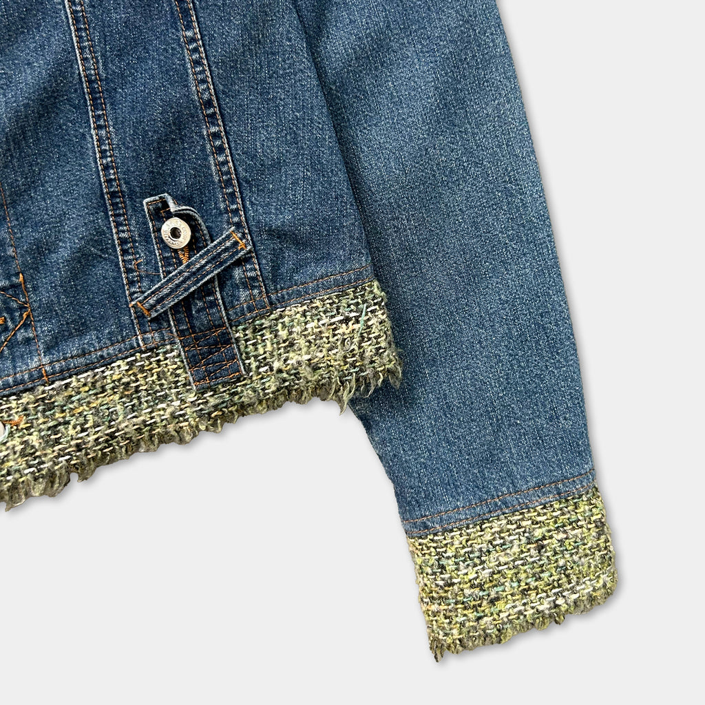A close-up view of a denim jacket with a fringed trim and a button closure.