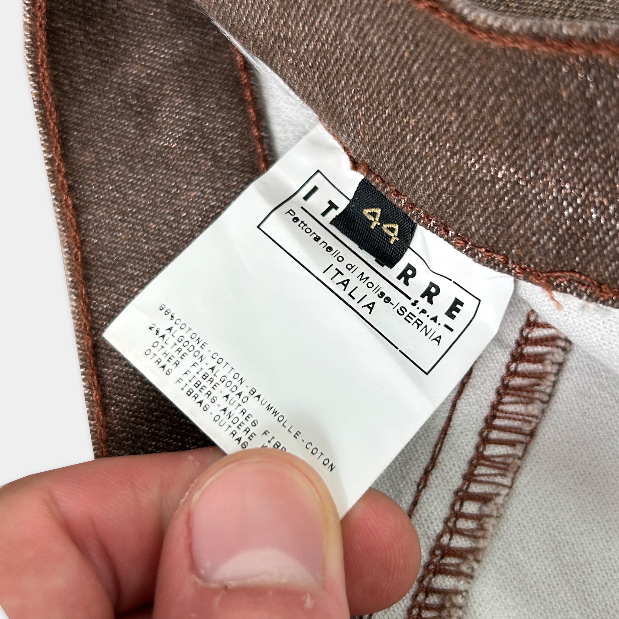 A person's hand holding a label with text on it, which appears to be a label for a piece of clothing.