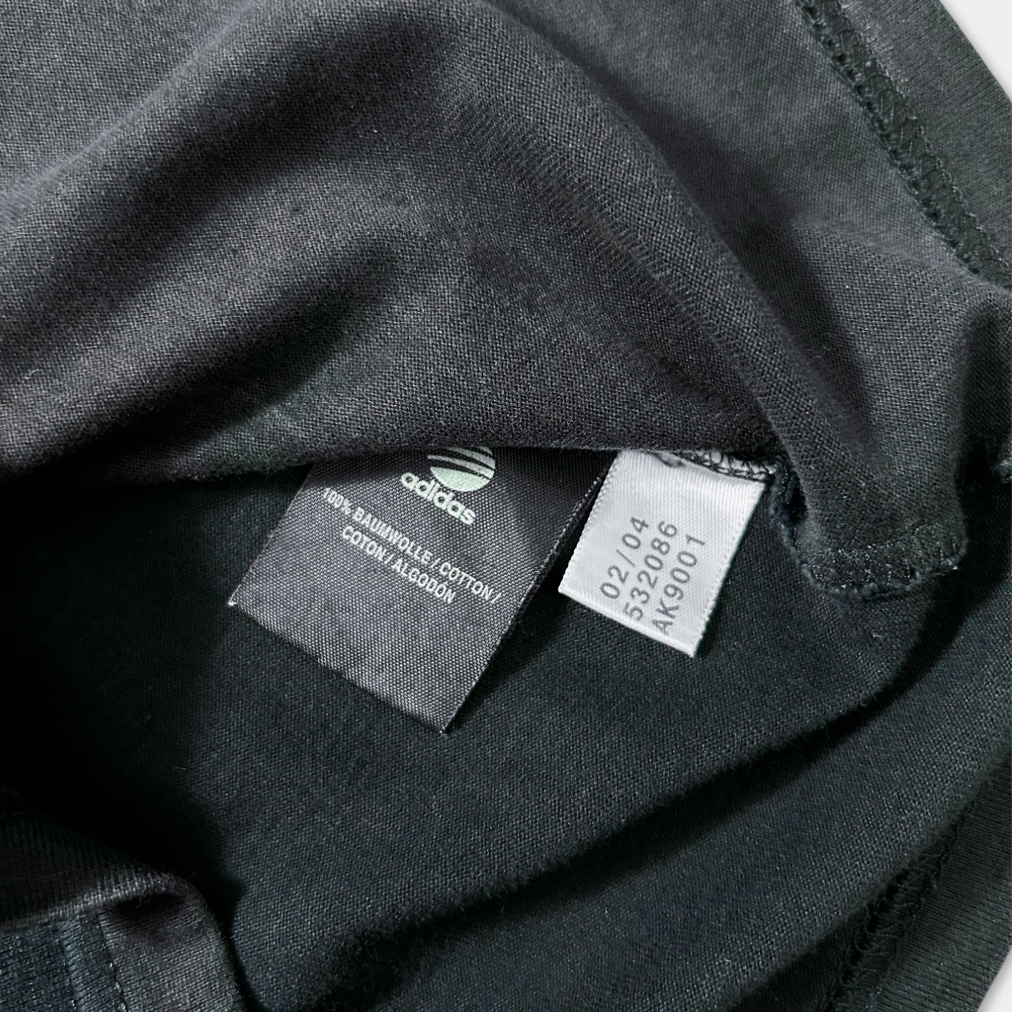 a close-up view of a black Adidas t-shirt, with a label attached to it.