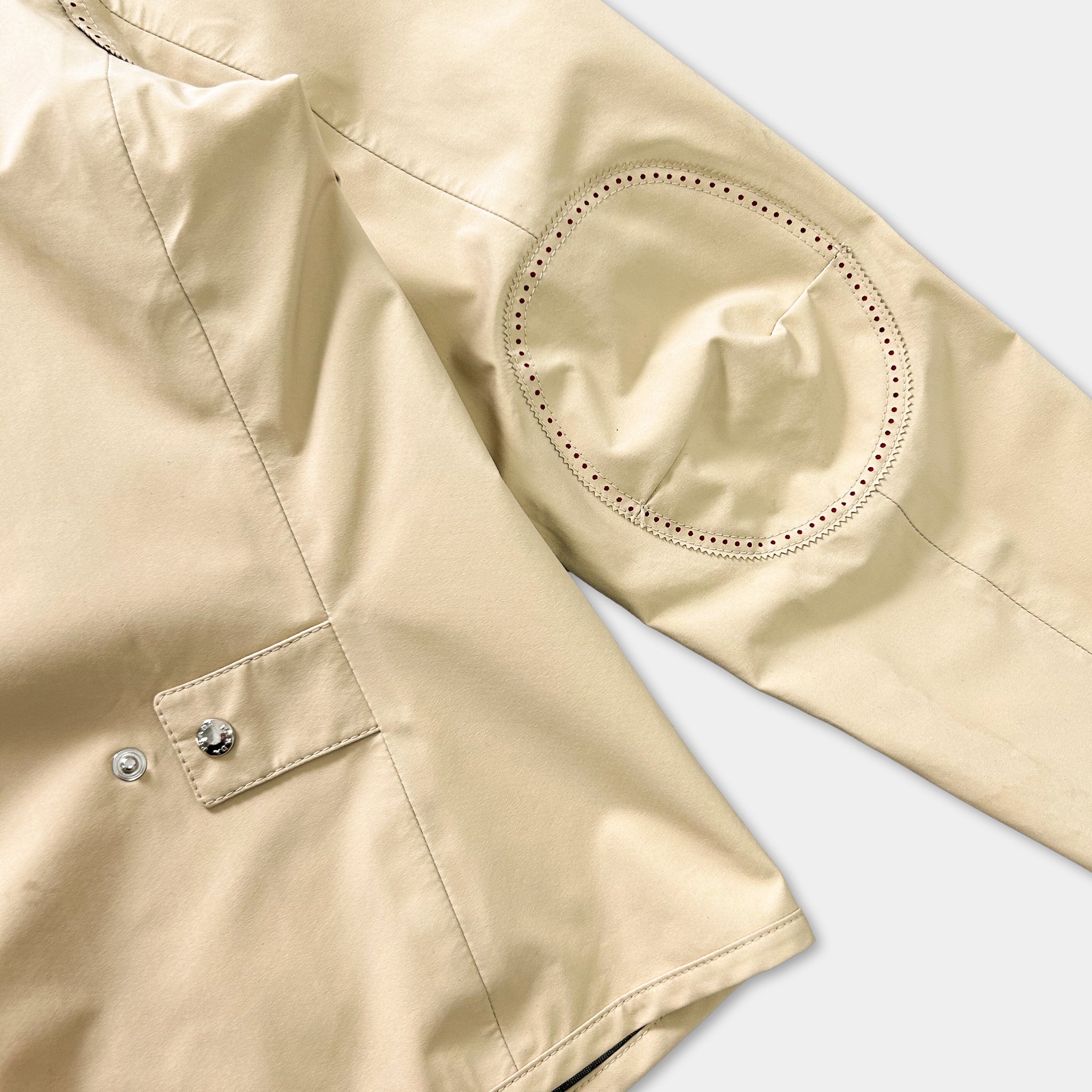 A close-up view of a beige jacket sleeve with a circular embroidered patch on the left side.