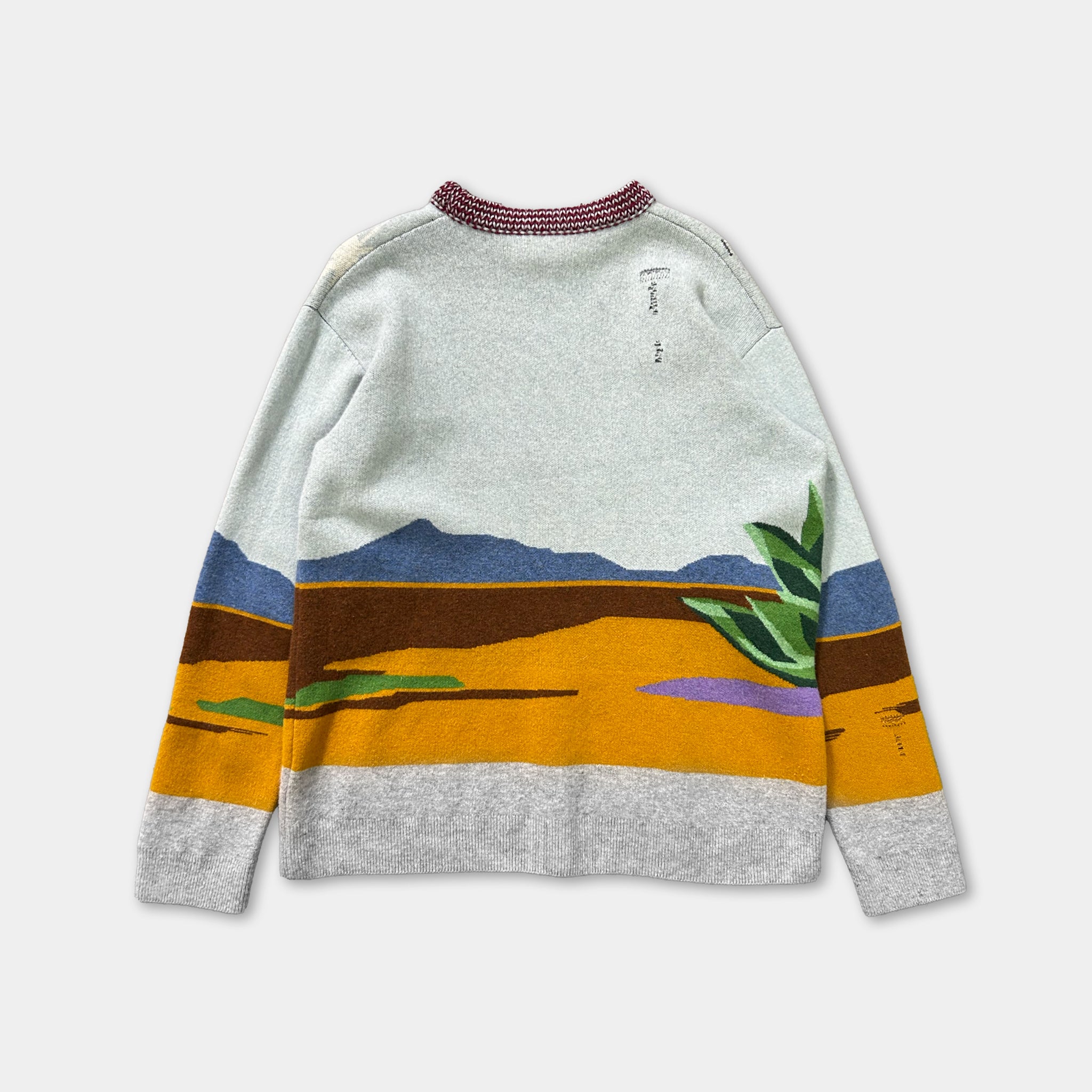 A gray and white sweater with a colorful landscape design on the front.