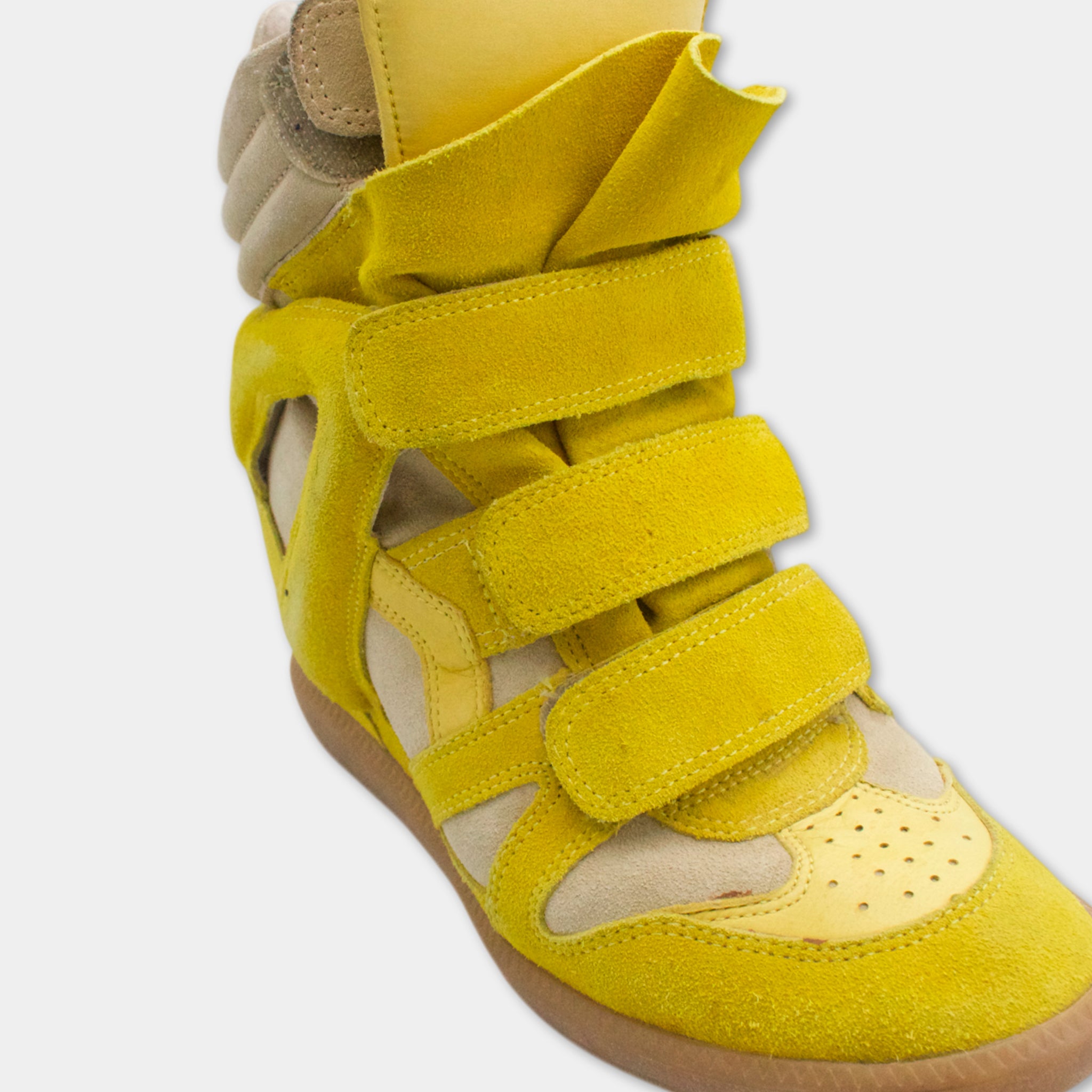 A close-up view of a yellow and beige high-top sneaker with multiple straps and a pointed toe.