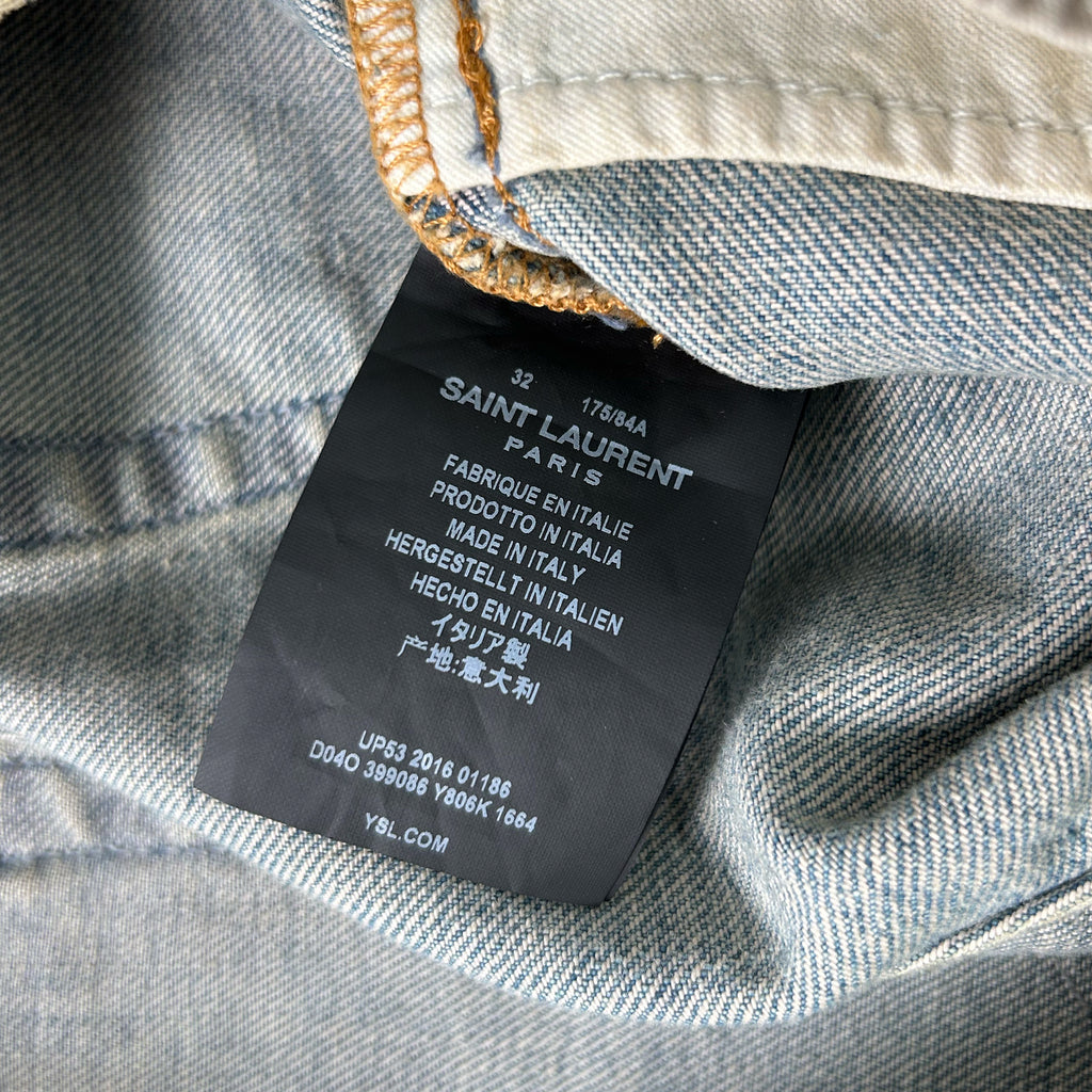 A close-up of a denim fabric, possibly a pair of jeans, with a label attached to it. The label appears to be a label from Saint Laurent, a French fashion brand.