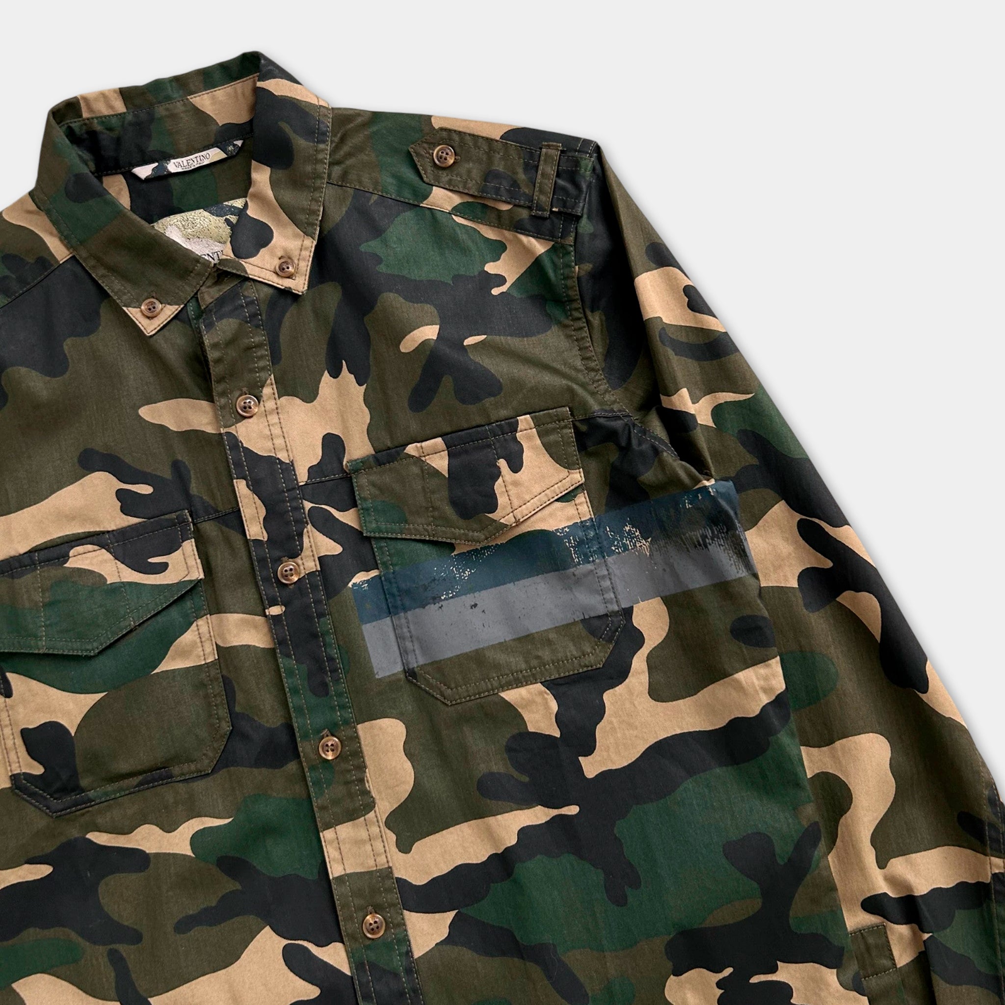A camouflage-patterned military-style shirt with a button-down front and multiple pockets.