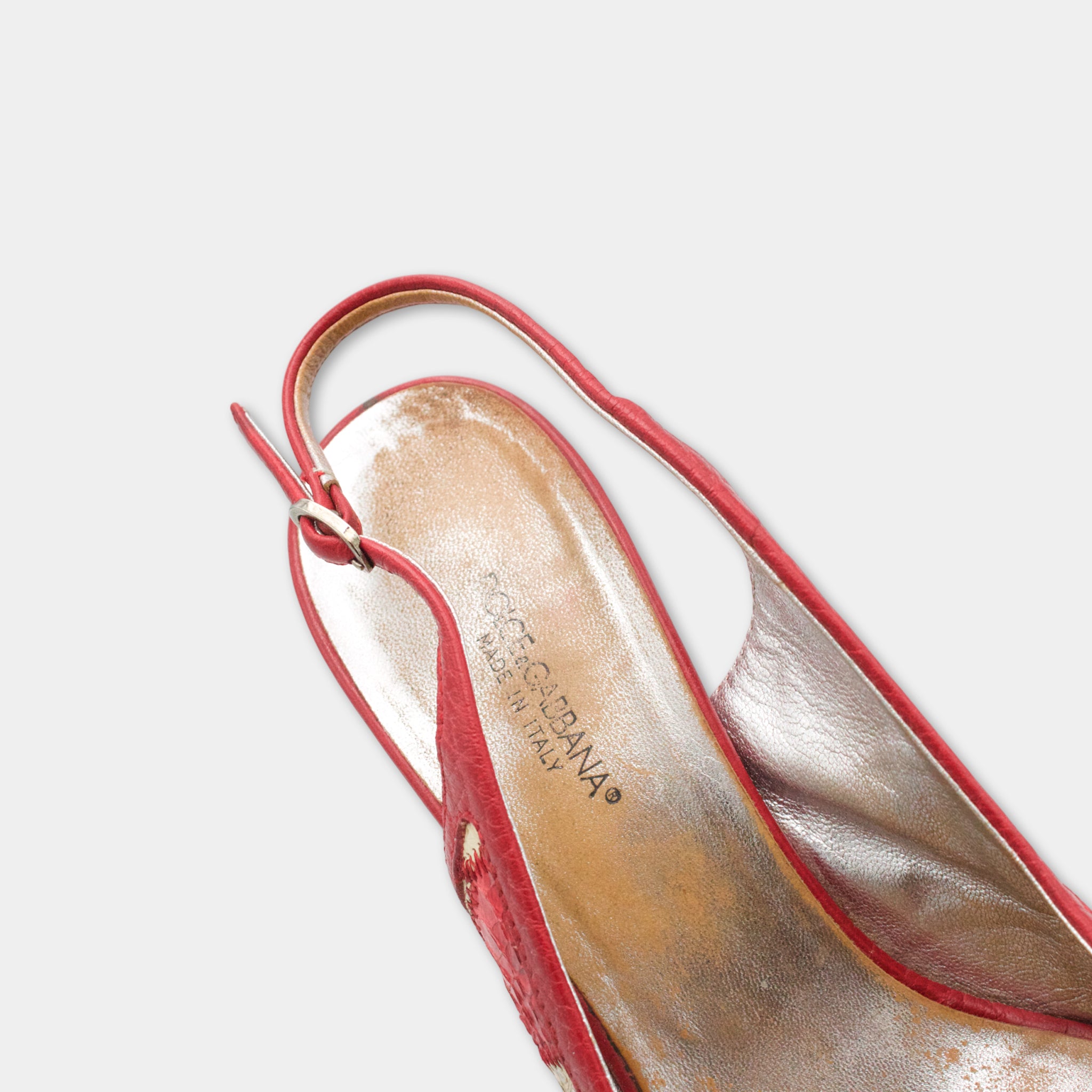 A close-up view of a red high-heeled shoe with a metallic sole and a strap.