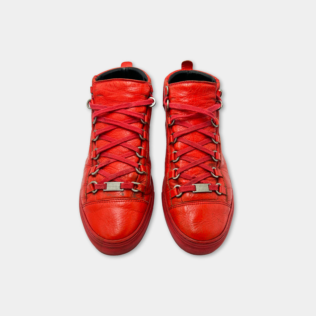 A pair of red high-top sneakers with red laces and metal studs on the sides.