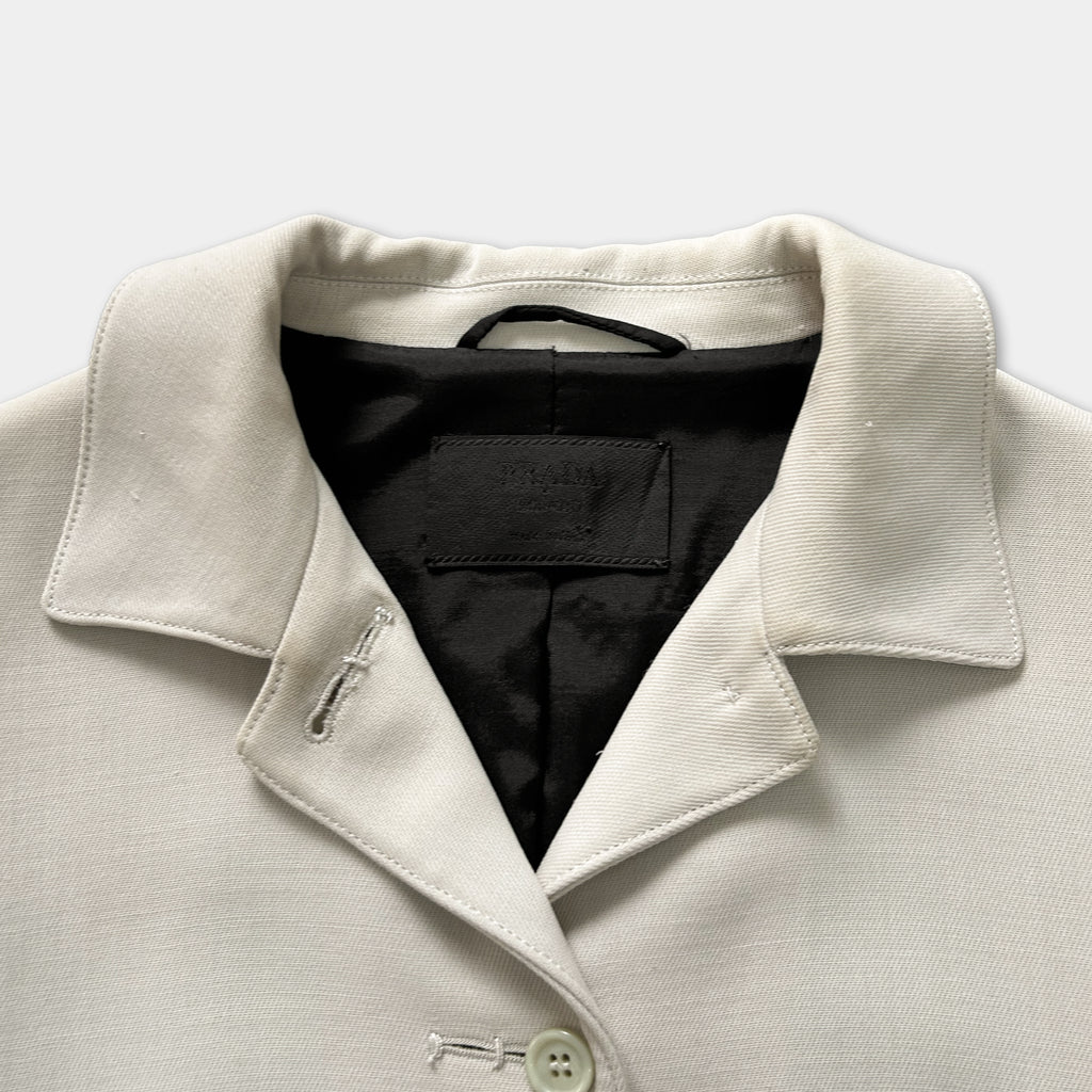 A close-up view of a cream-colored jacket with a black collar and a black label on the front.