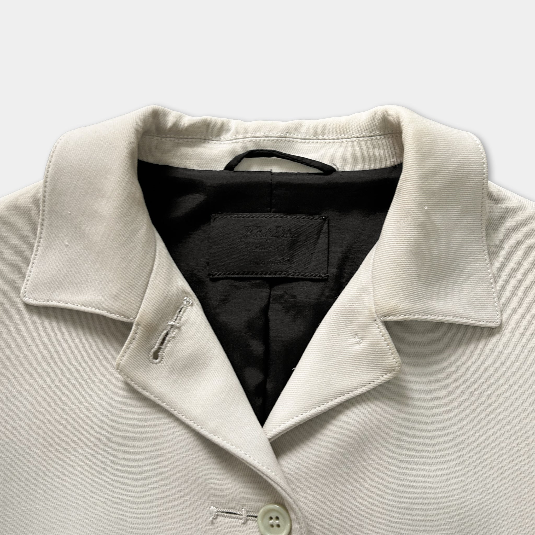 A close-up view of a cream-colored jacket with a black collar and a black label on the front.
