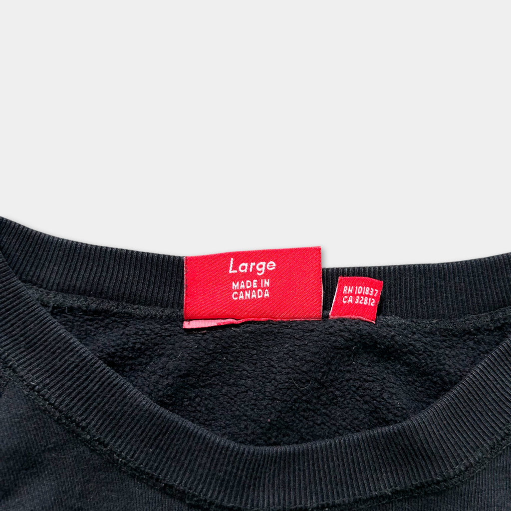 A black sweater with a red label on the collar that reads "Large Made in Canada".