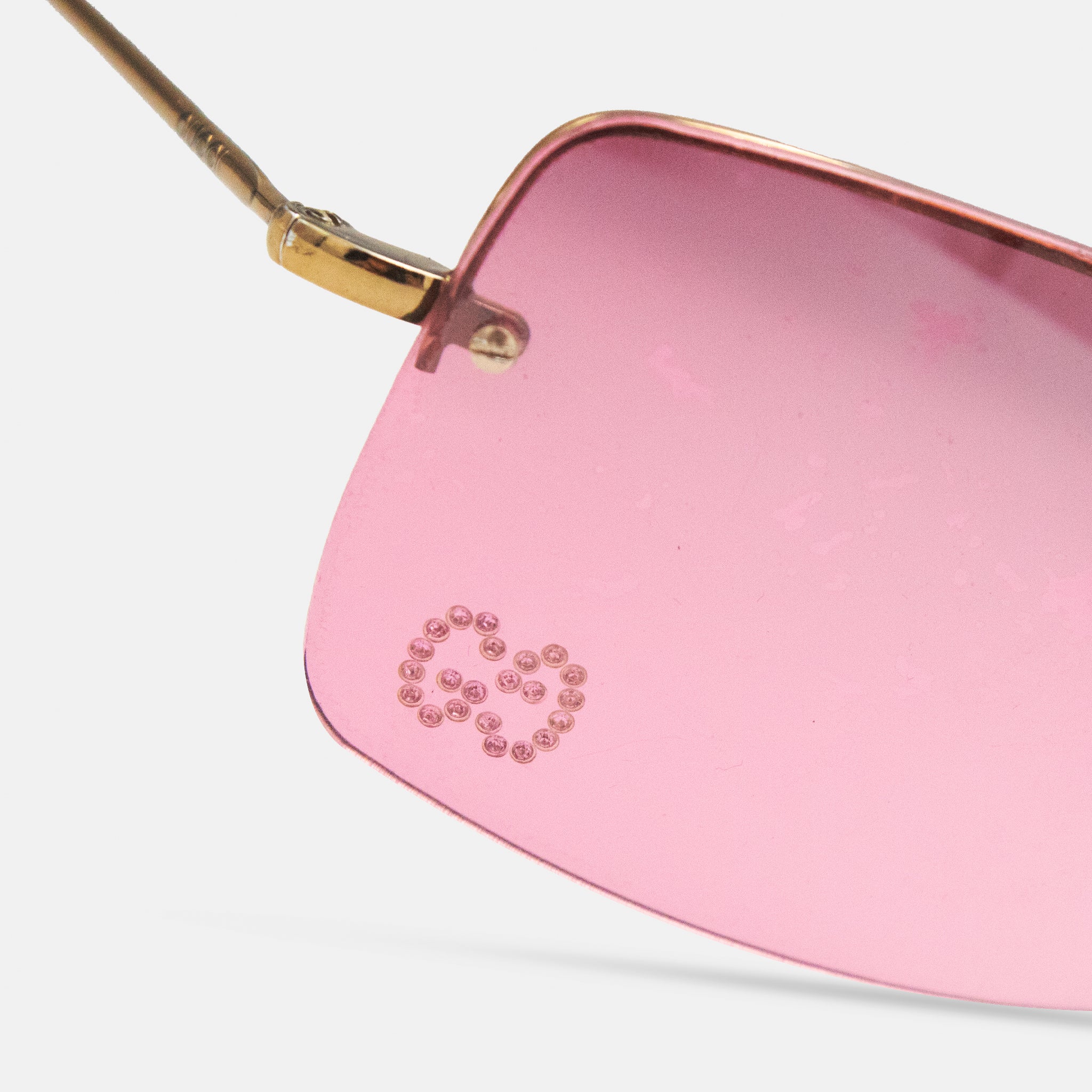 A close-up view of a pair of pink sunglasses with a gold frame and a small logo or symbol on the lens.