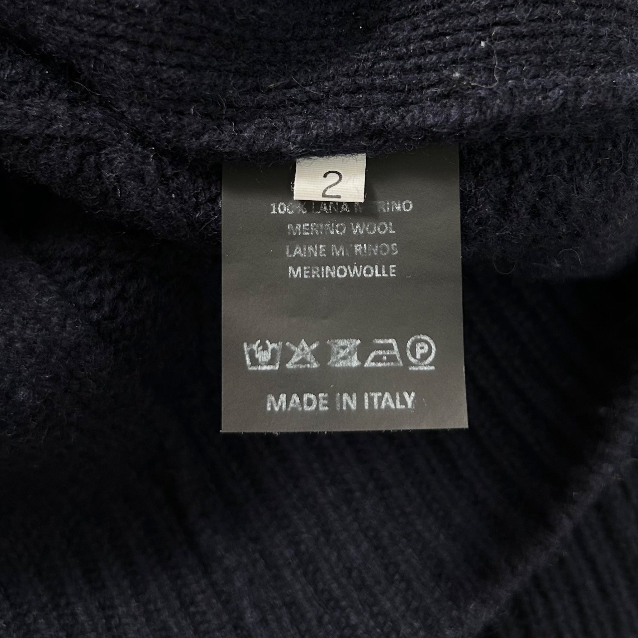 a close-up view of a black fabric, possibly a sweater or a garment, with a label attached to it. The label contains text and symbols, indicating the material, care instructions, and the fact that the item is made in Italy.