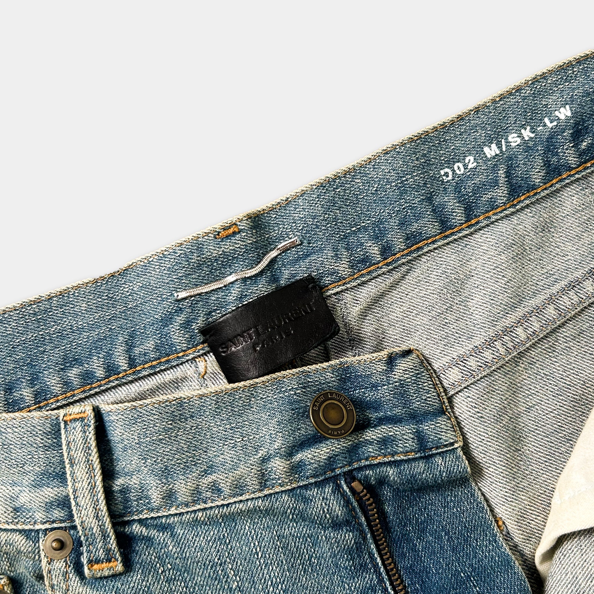 A close-up view of a pair of blue jeans, showing the zipper, pocket, and belt.