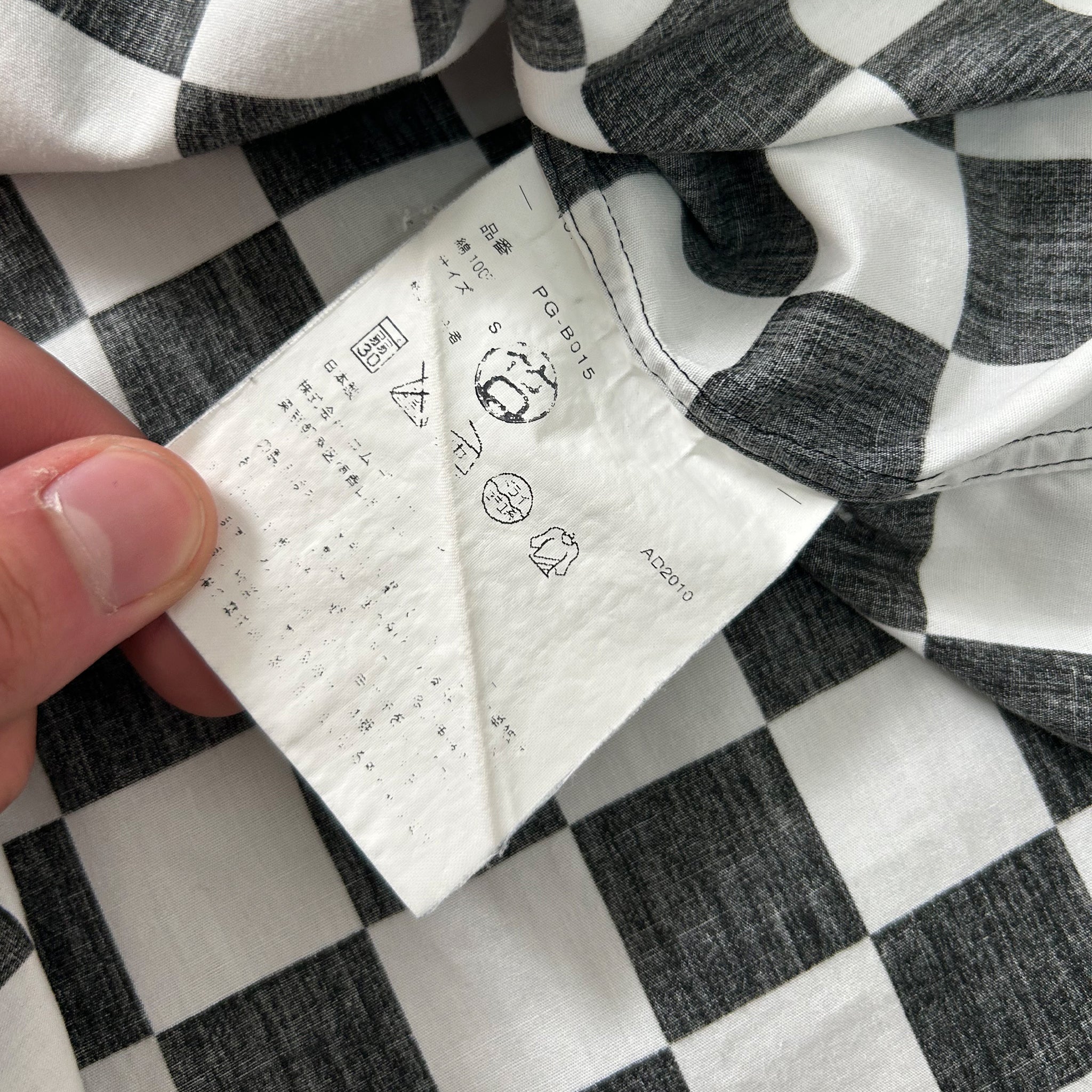 A hand is holding a piece of paper with text and symbols on it, which appears to be a label or receipt.
