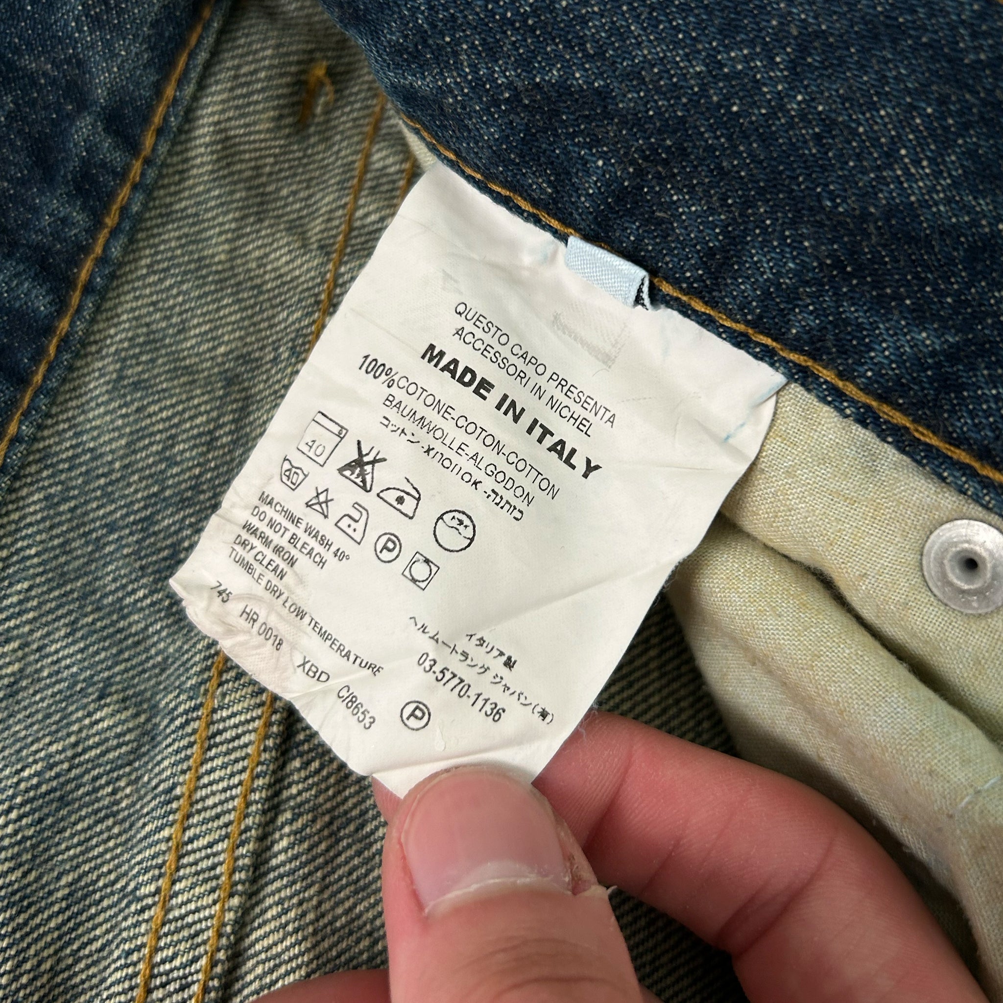 A person's hand holding a denim fabric label with text and symbols, indicating the material and care instructions for the fabric.
