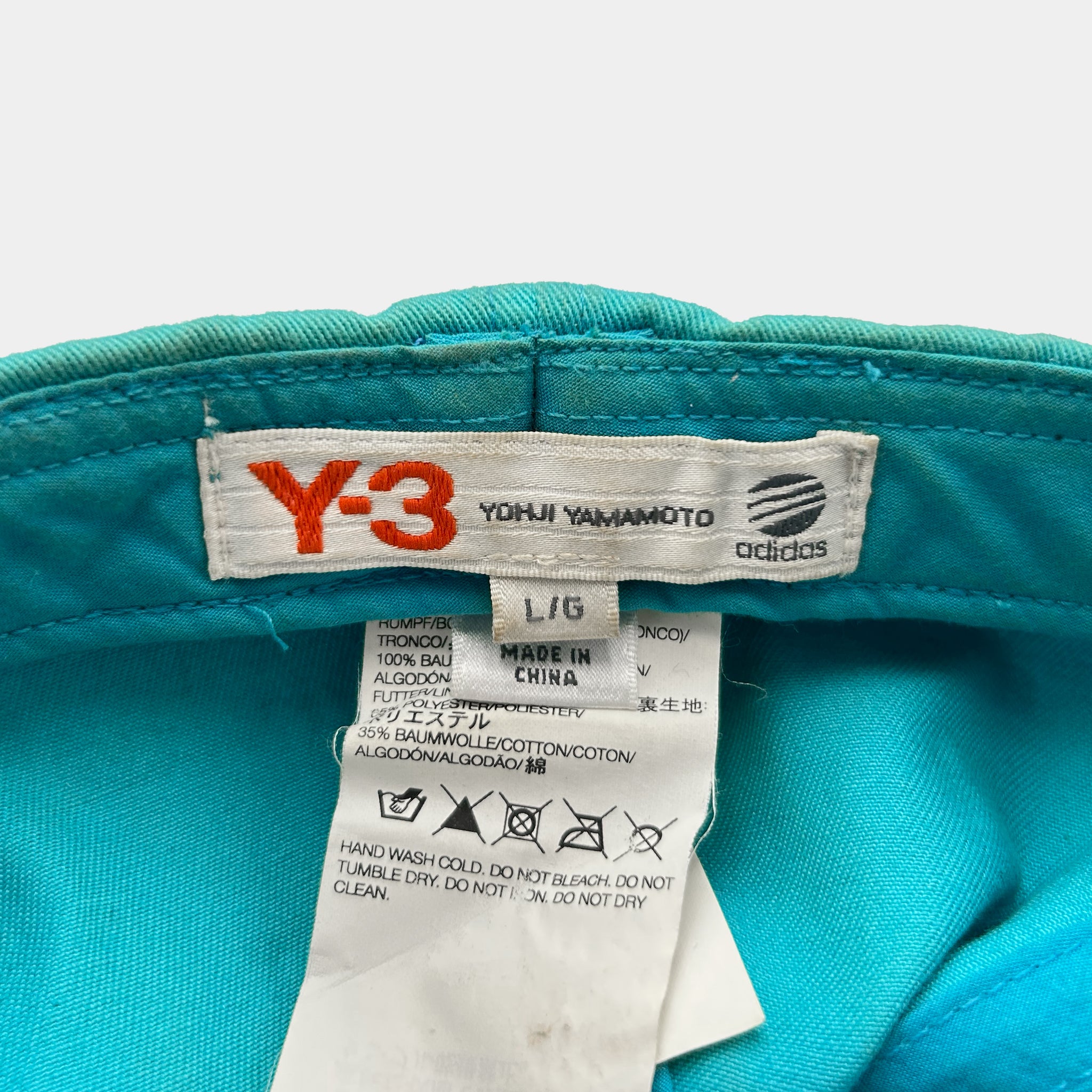 a close-up view of a blue fabric, possibly a piece of clothing, with a label attached to it. The label appears to be a product label from an Adidas brand, indicating the brand name, size, and other details.