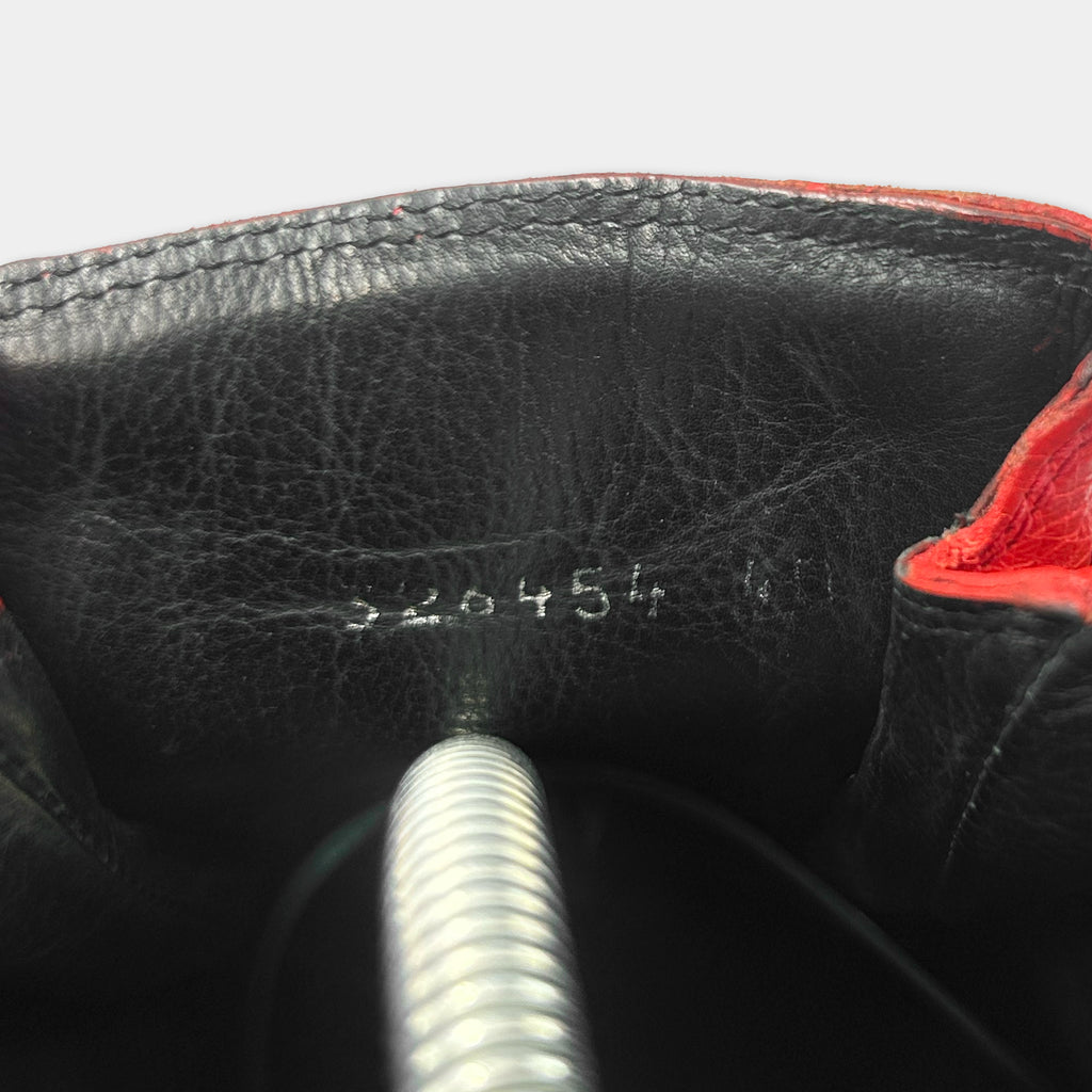 the interior of a black leather shoe, with a red trim. There is a metal spring protruding from the shoe, and the sole of the shoe is visible.