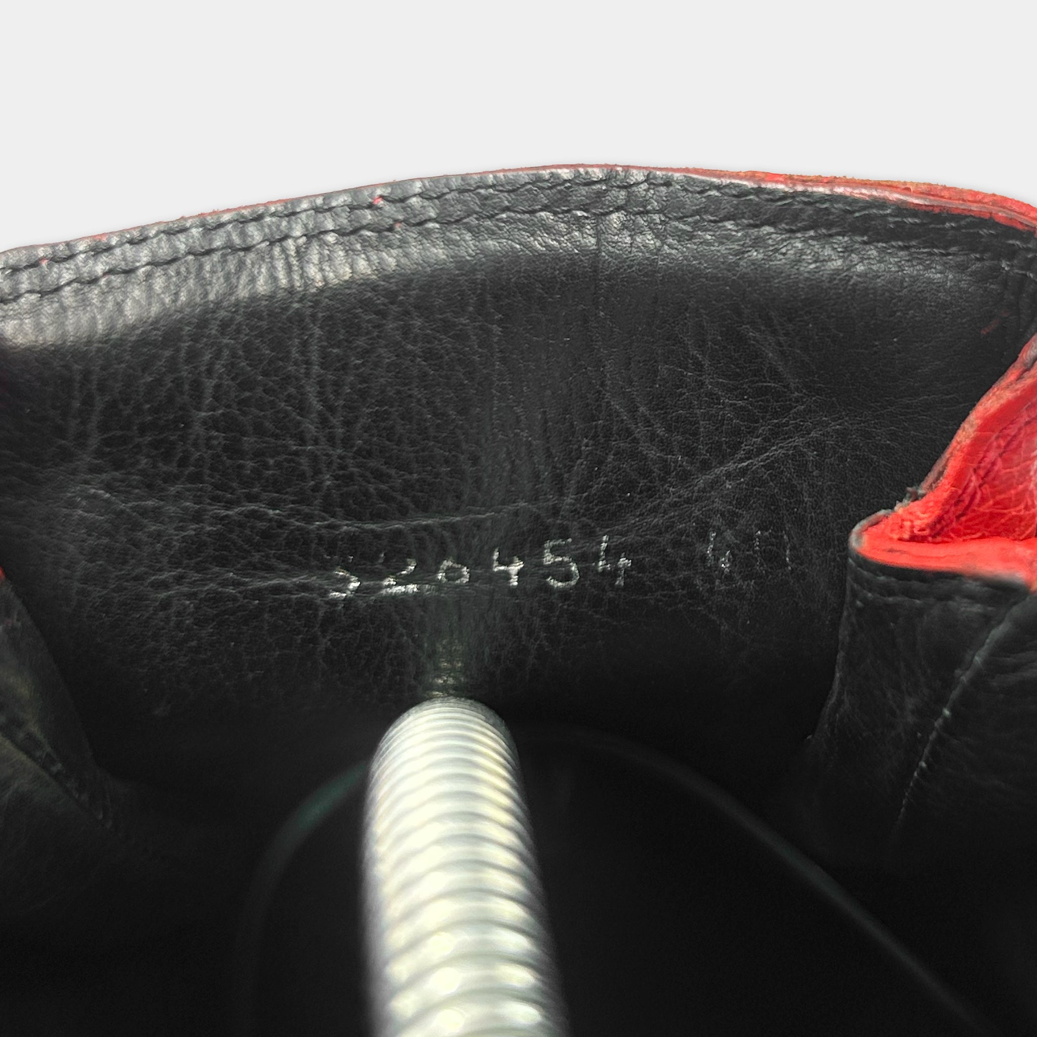 the interior of a black leather shoe, with a red trim. There is a metal spring protruding from the shoe, and the sole of the shoe is visible.