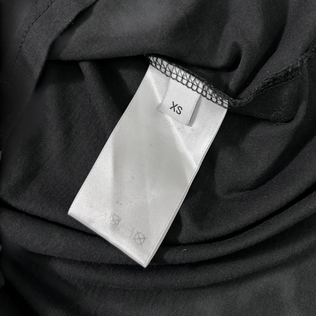 A close-up view of a white label with the text "XS" printed on it, attached to a black fabric.