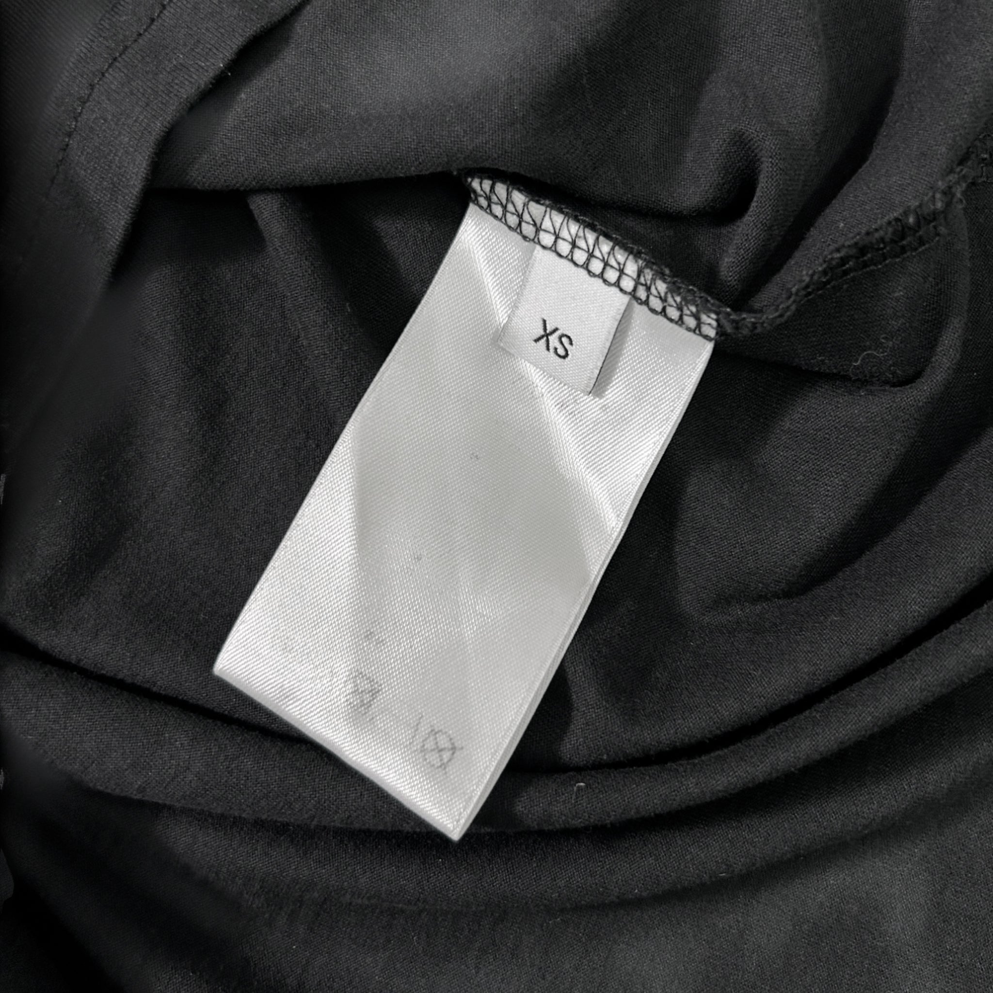 A close-up view of a white label with the text "XS" printed on it, attached to a black fabric.