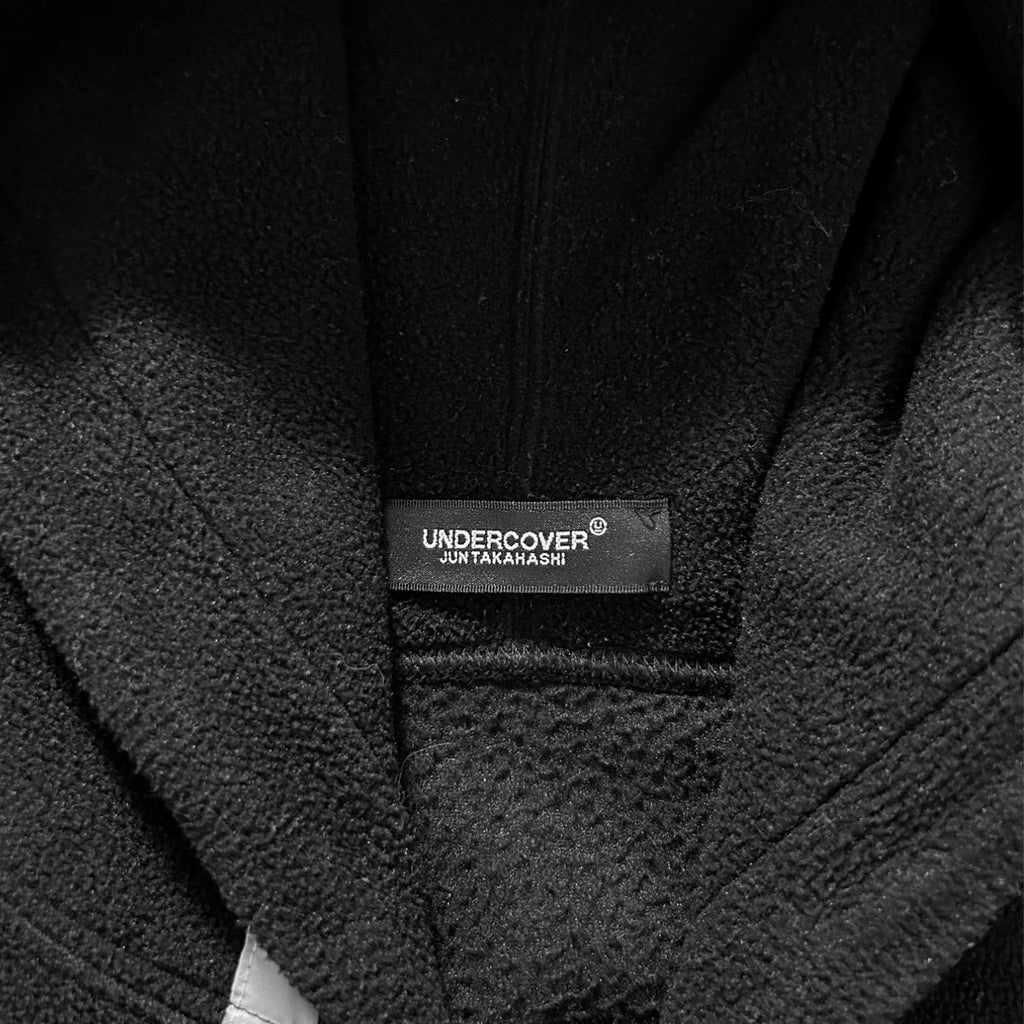 a close-up view of a black hoodie or jacket with a label that reads "UNDERCOVER" and "JAPAN".