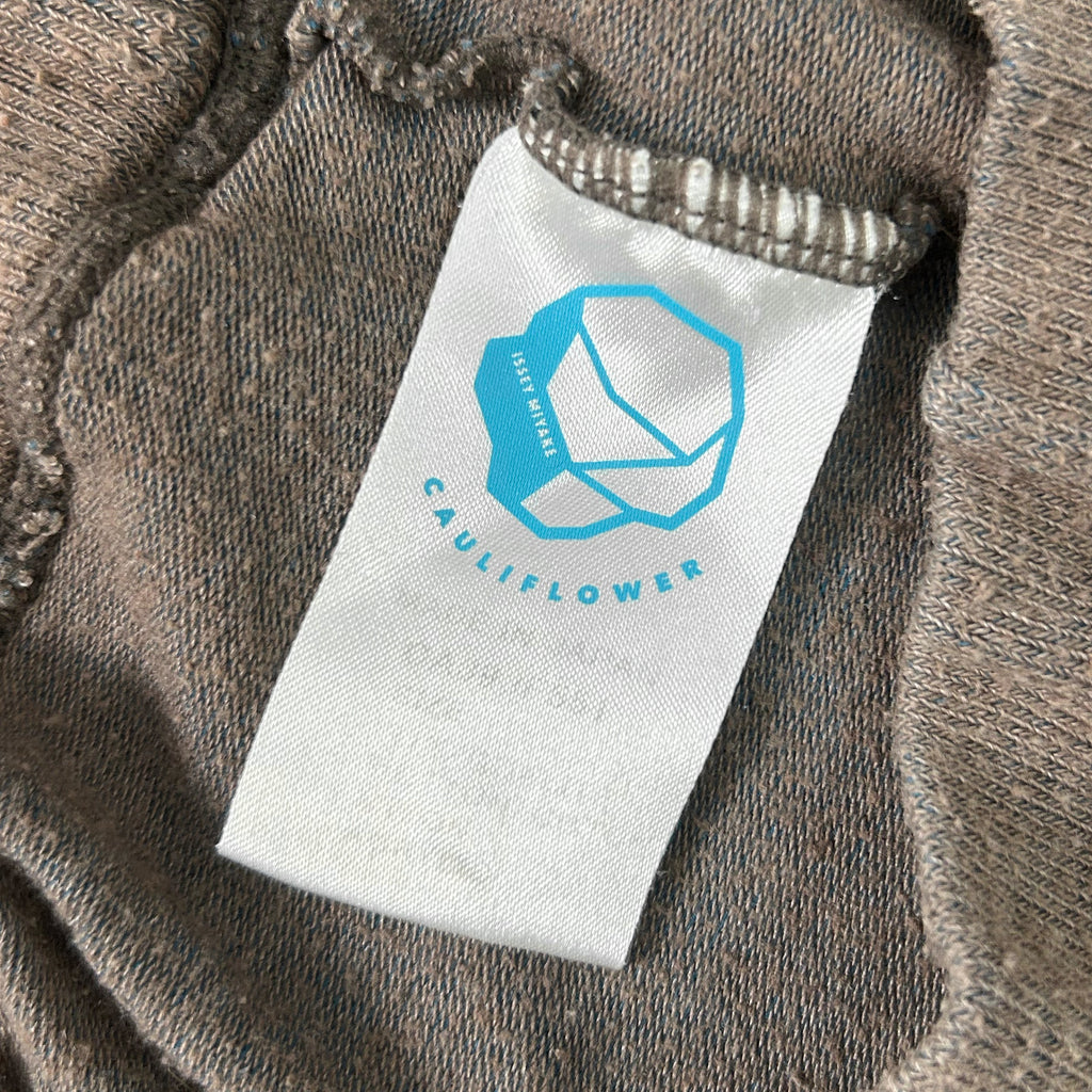 a close-up view of a white label with a blue logo on a piece of clothing, specifically a grey sweater.