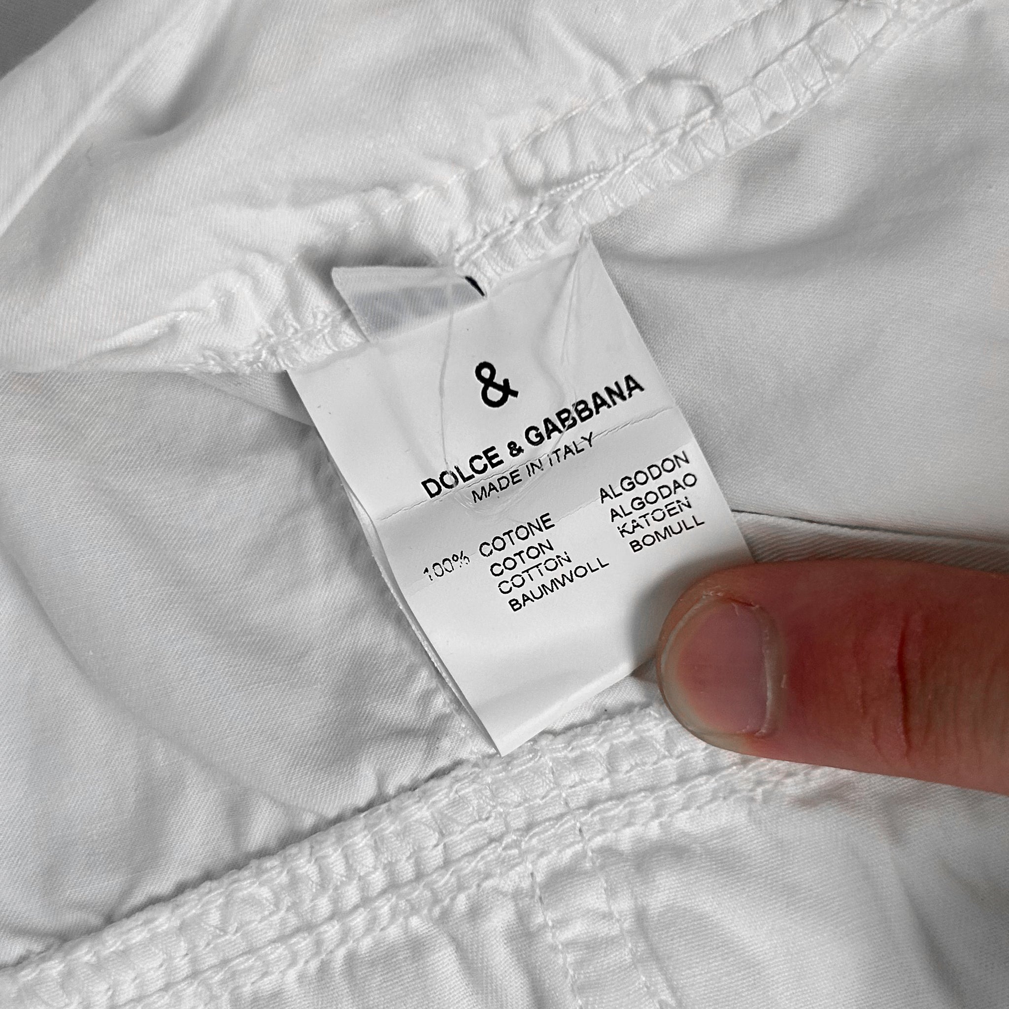 A close-up of a white fabric label from Dolce & Gabbana, with a person's finger pointing to it.