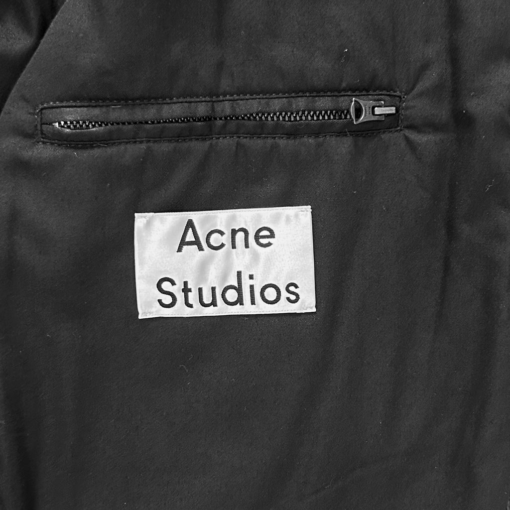 a close-up view of a black fabric with a white label attached to it, displaying the text "Acne Studios".