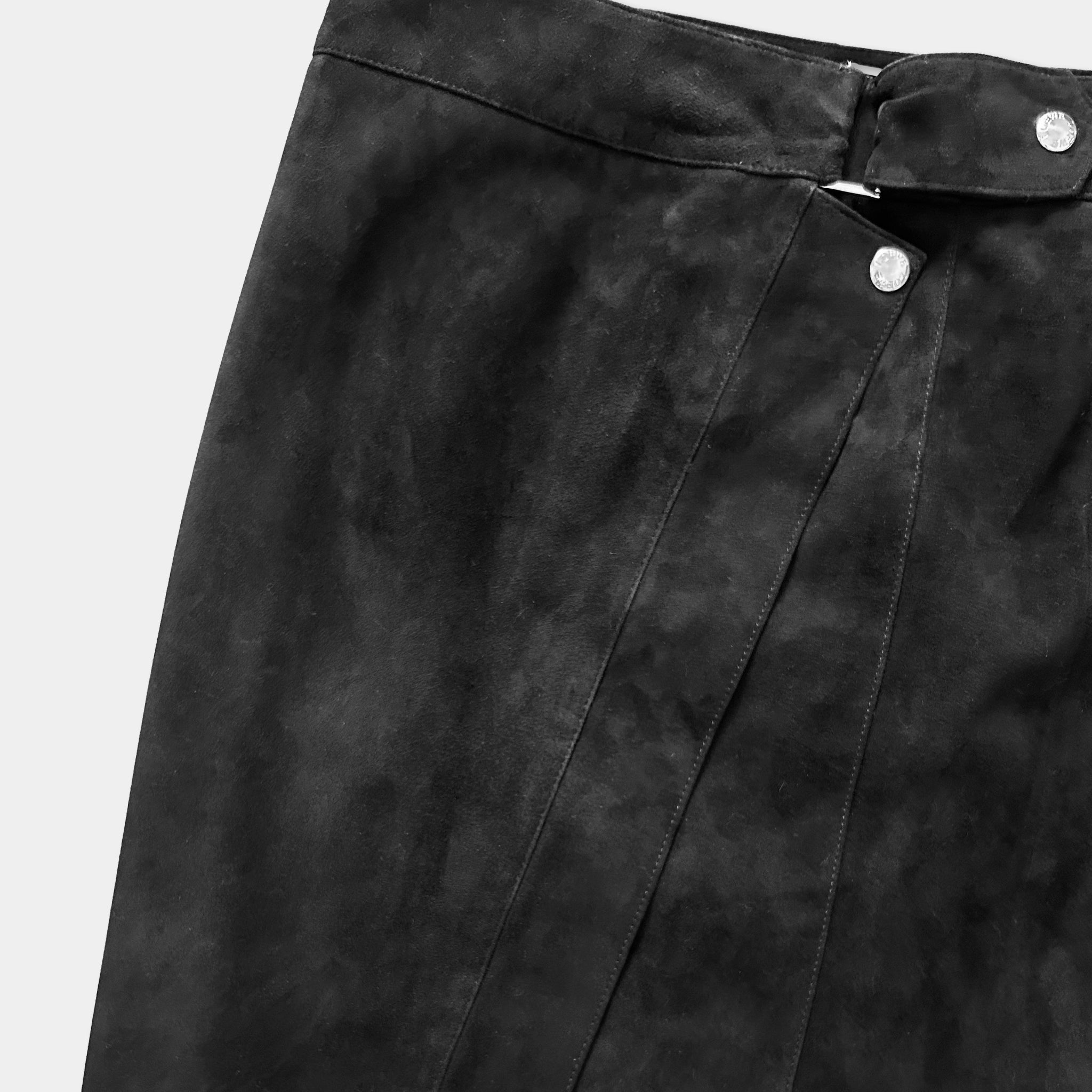 A close-up view of a black, pleated skirt with a button closure.