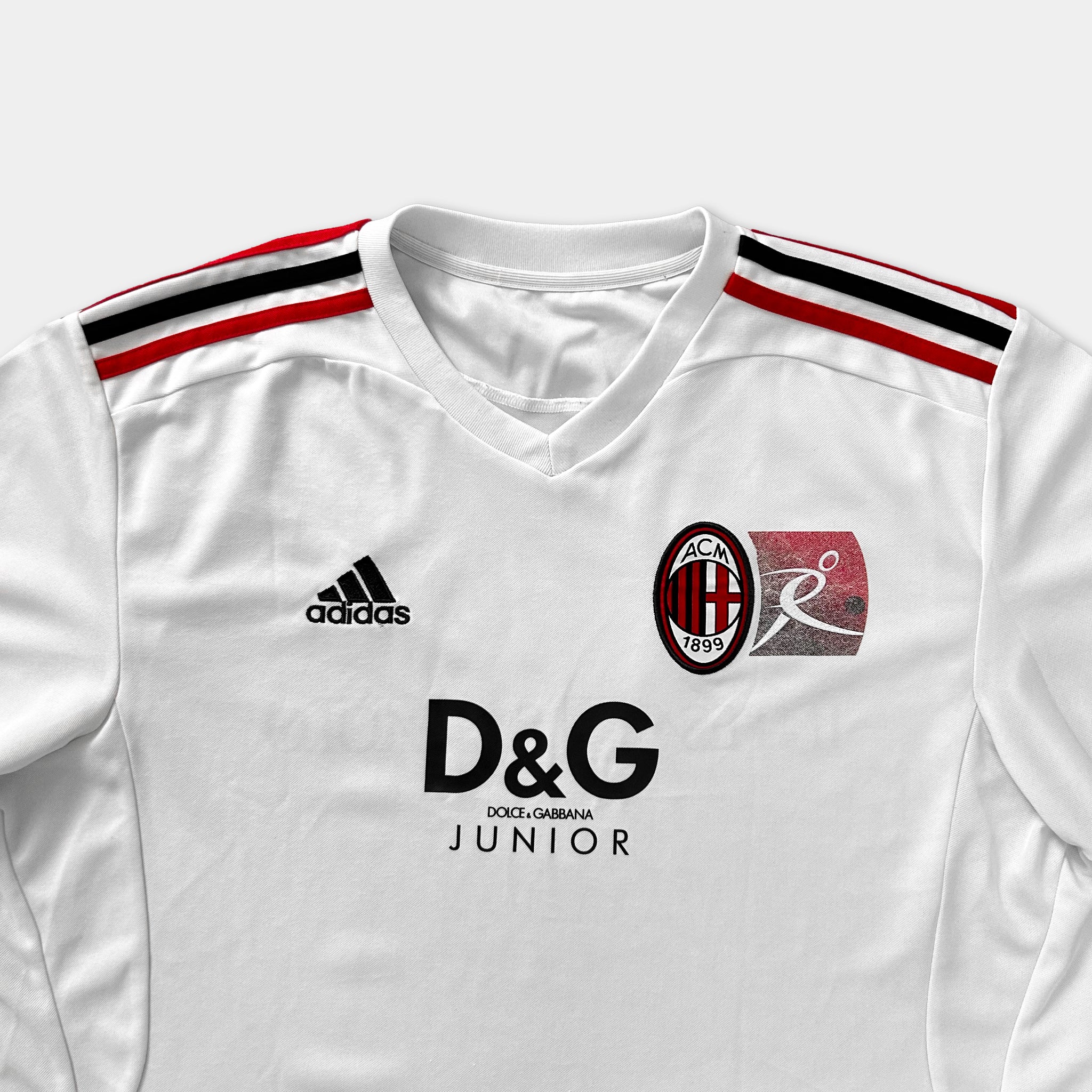 A white soccer jersey with red and black stripes, featuring the Adidas logo, the D&G logo, and the ACM logo.