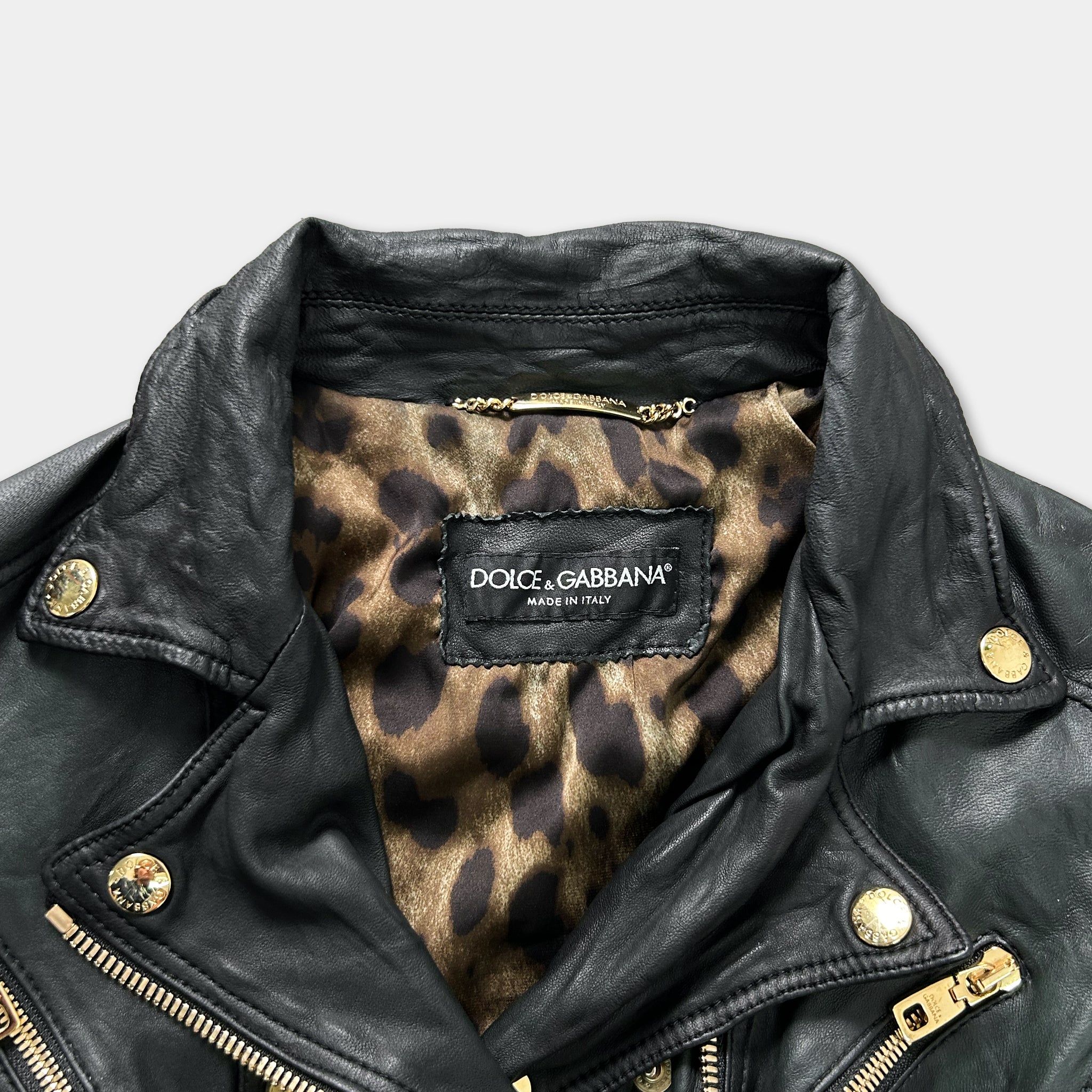 A close-up view of a black leather jacket with a leopard print lining, featuring a label that reads "DOLCE & GABBANA" and "Made in Italy".