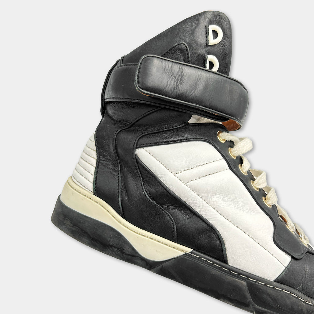 A close-up view of a black and white high-top sneaker with a black strap and white sole.