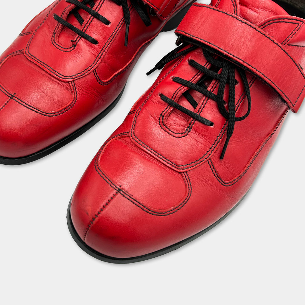 A pair of red leather shoes with black laces and a black strap.