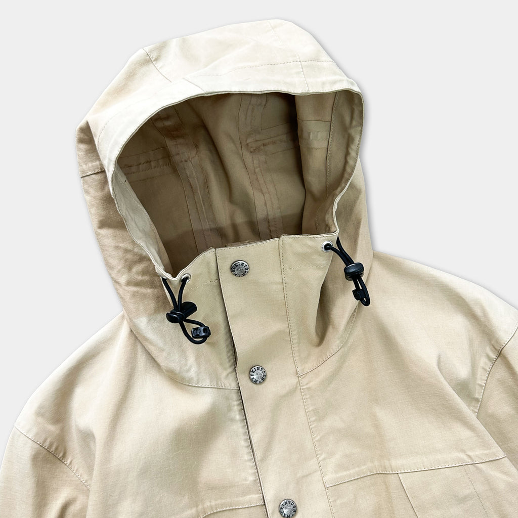 A beige jacket with a hood and buttons, featuring a black zipper and drawstring hood.